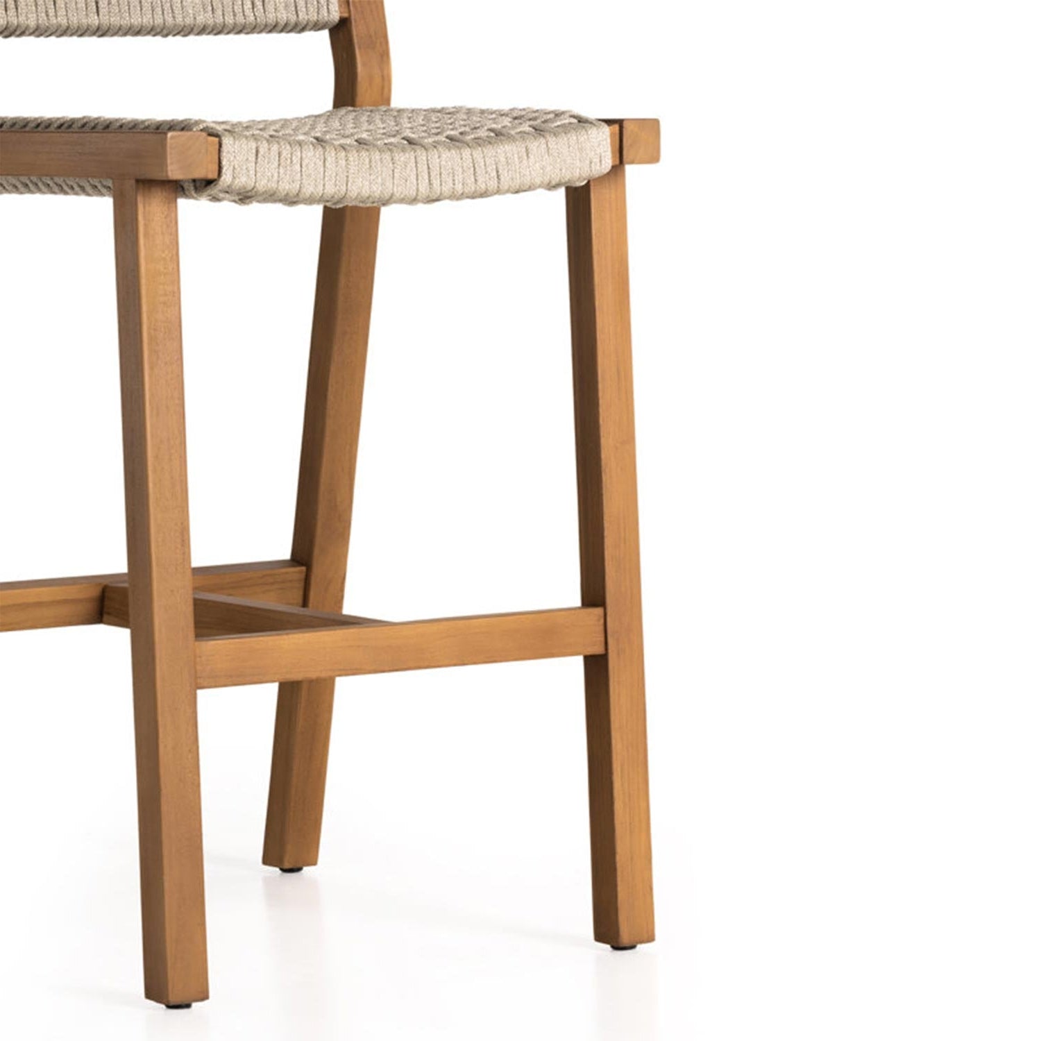 Close-up of an armless outdoor bar stool showing natural teak legs, cross-stretcher support and a woven neutral-beige seat in a coastal style.