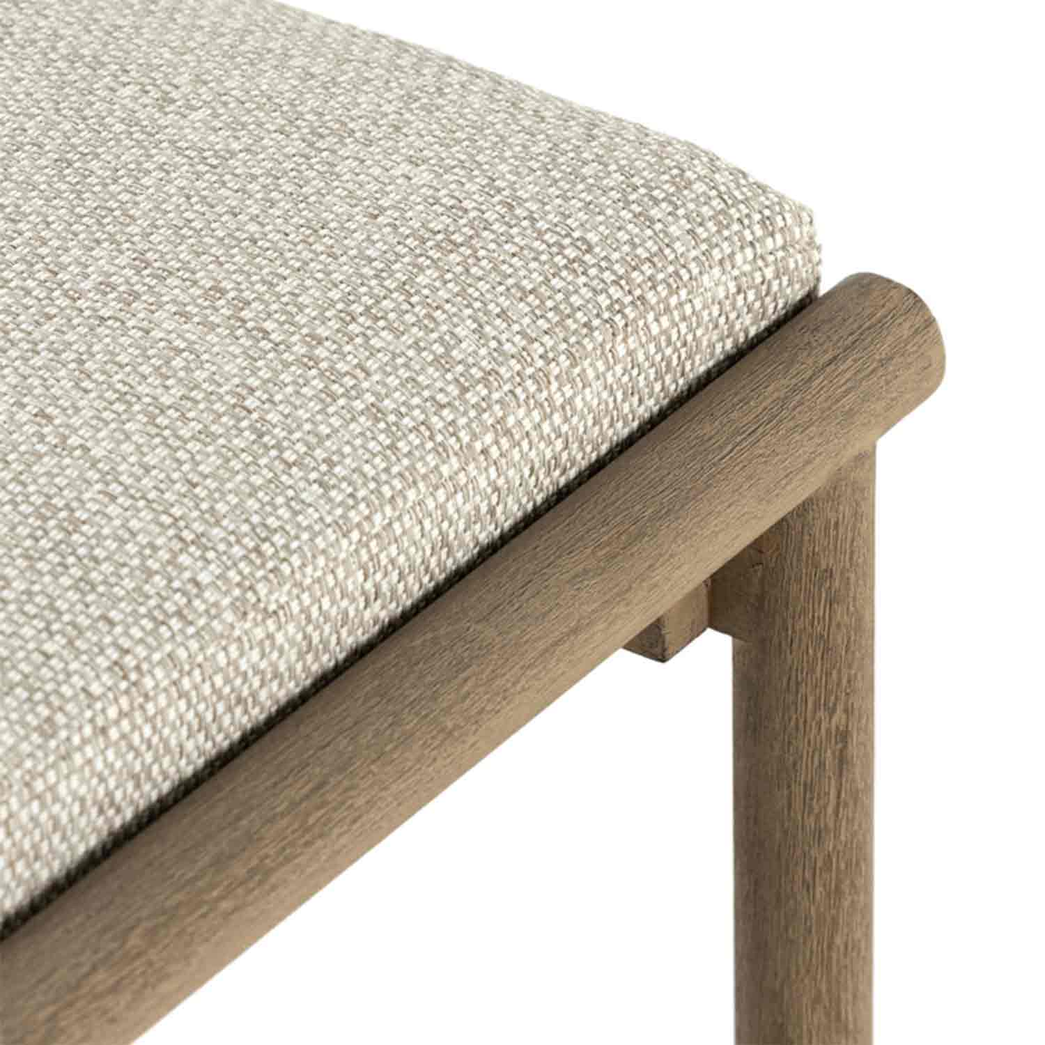 Close-up of a beige woven upholstered seat cushion on a teak outdoor bar stool, showing the textured fabric, rounded teak rail and part of the teak leg.