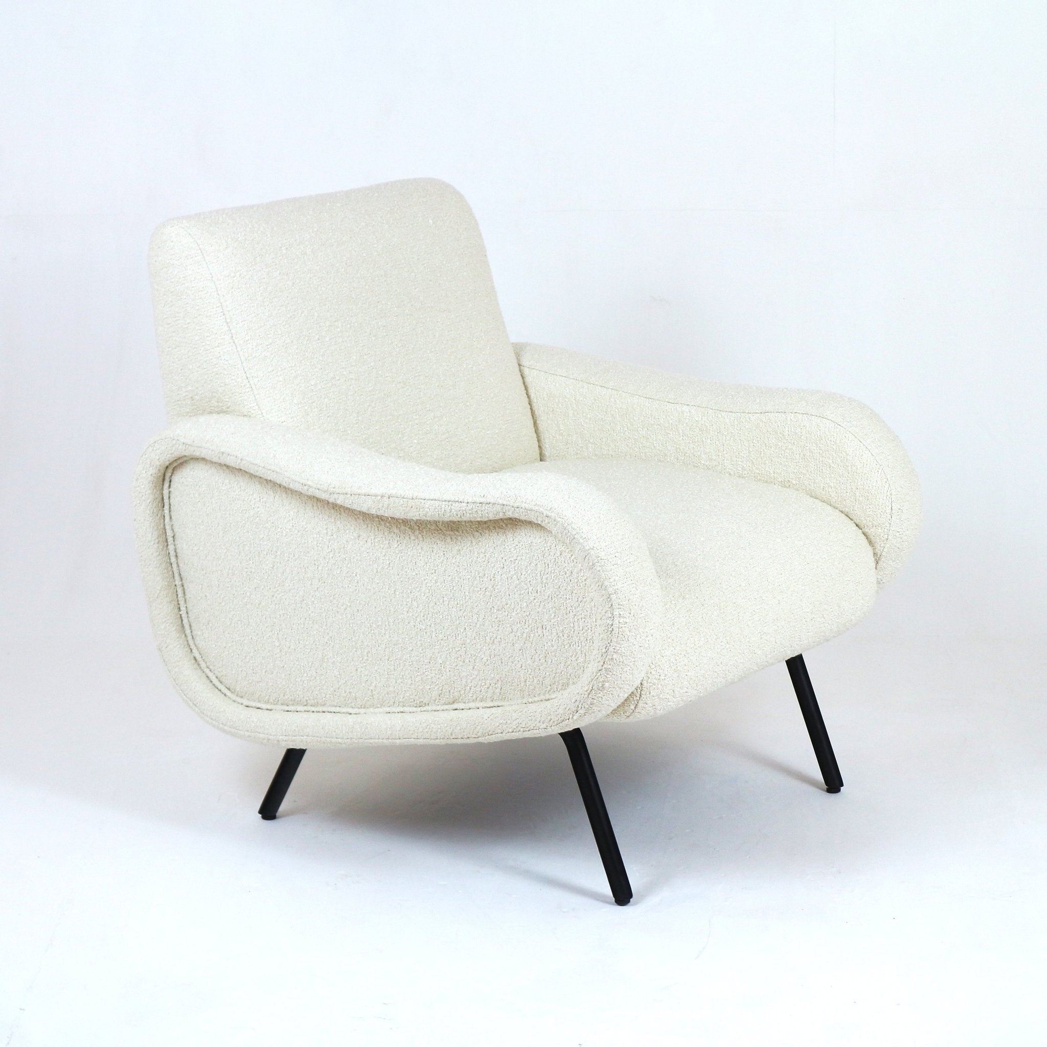 Low-back modern armchair upholstered in white boucle fabric with sculpted curved arms and a cushioned seat, supported by slender black metal legs.