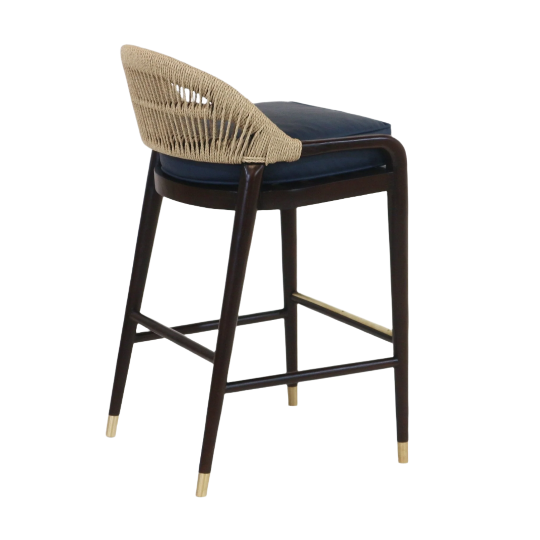 Teak-framed bar stool shown at a three-quarter rear angle with a woven natural rope back, blue upholstered seat cushion, tapered dark wood legs, brass-capped feet and a brass footrest.