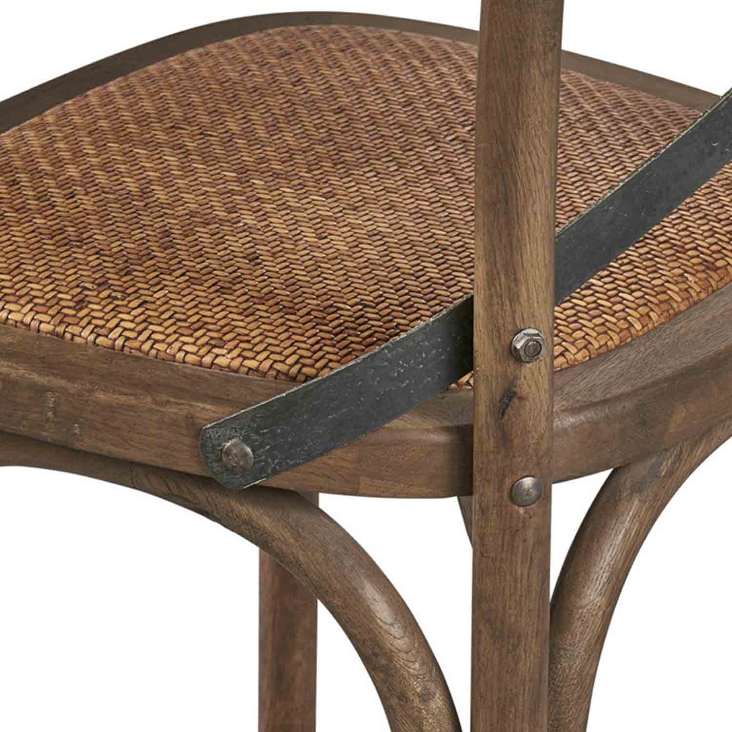 Close-up of a natural woven seat on a teak outdoor bar stool showing curved teak legs, a dark metal support strap with visible rivets, and textured wood grain in a coastal finish.