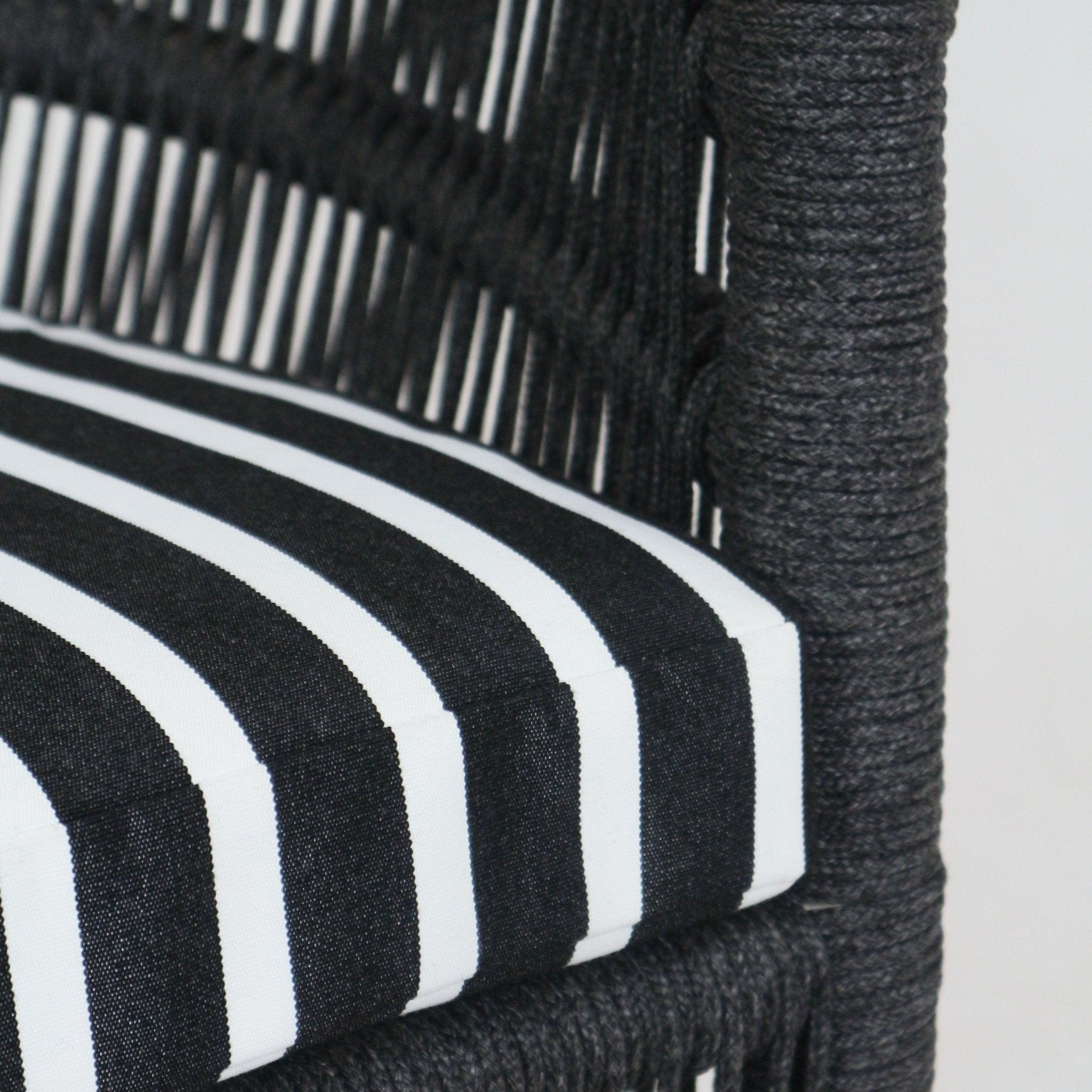 Close-up of a black-and-white striped Sunbrella seat cushion seated in a dark woven rope outdoor chair frame, highlighting the textured braided cord wrap and the crisp cushion edge.
