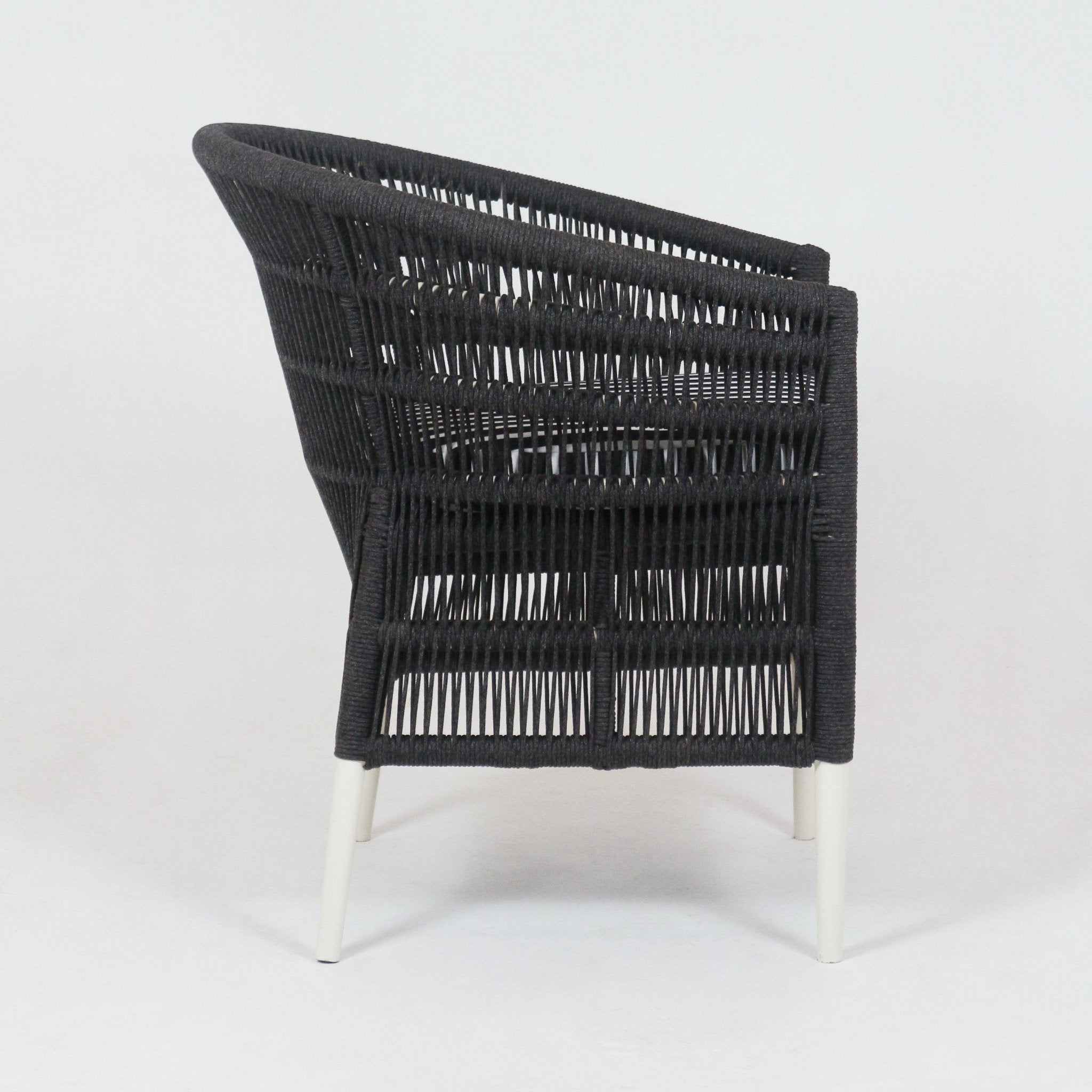 Side view of a dark woven-rope outdoor armchair with open lattice weave, gently sloped back, and slim white powder-coated metal legs.