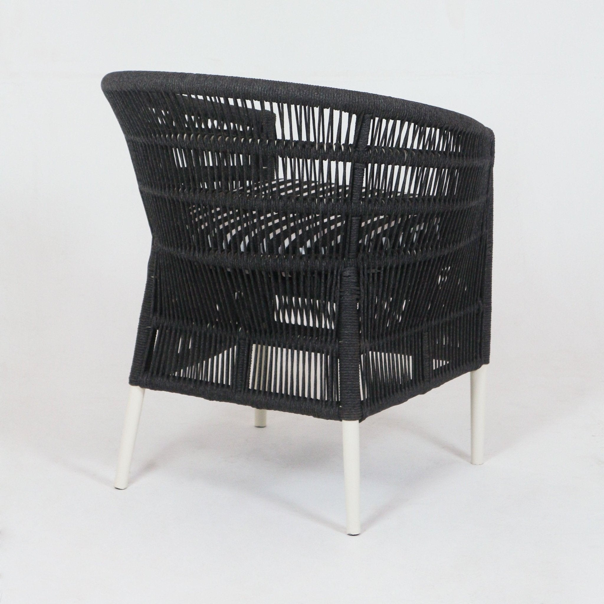 Three-quarter rear view of a coastal-style outdoor accent chair with dark woven rope back and sides over a metal frame and slim white powder-coated metal legs.