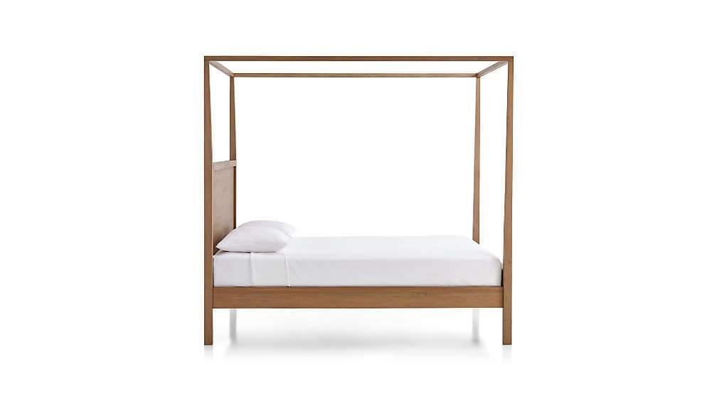 Midcentury teak four-poster bed in a natural wood finish with slim square posts and low platform frame, shown with a white mattress and pillow on a plain white background.