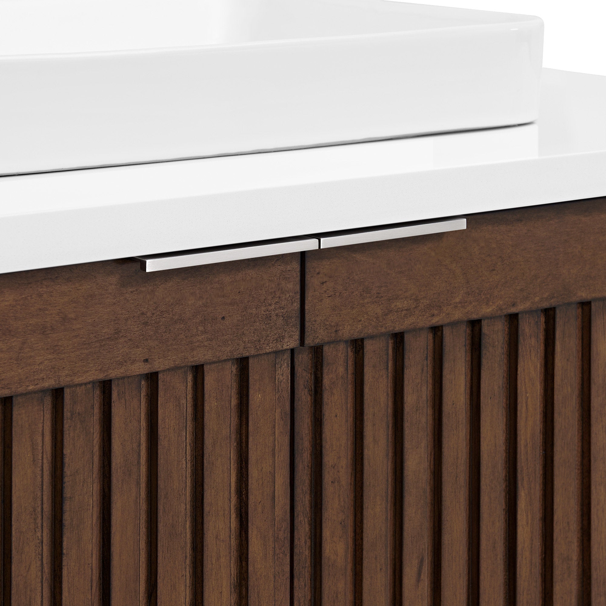 Close-up of a white stone countertop and rectangular ceramic vessel sink above a brown solid wood fluted vanity front with slim brushed metal drawer handles.