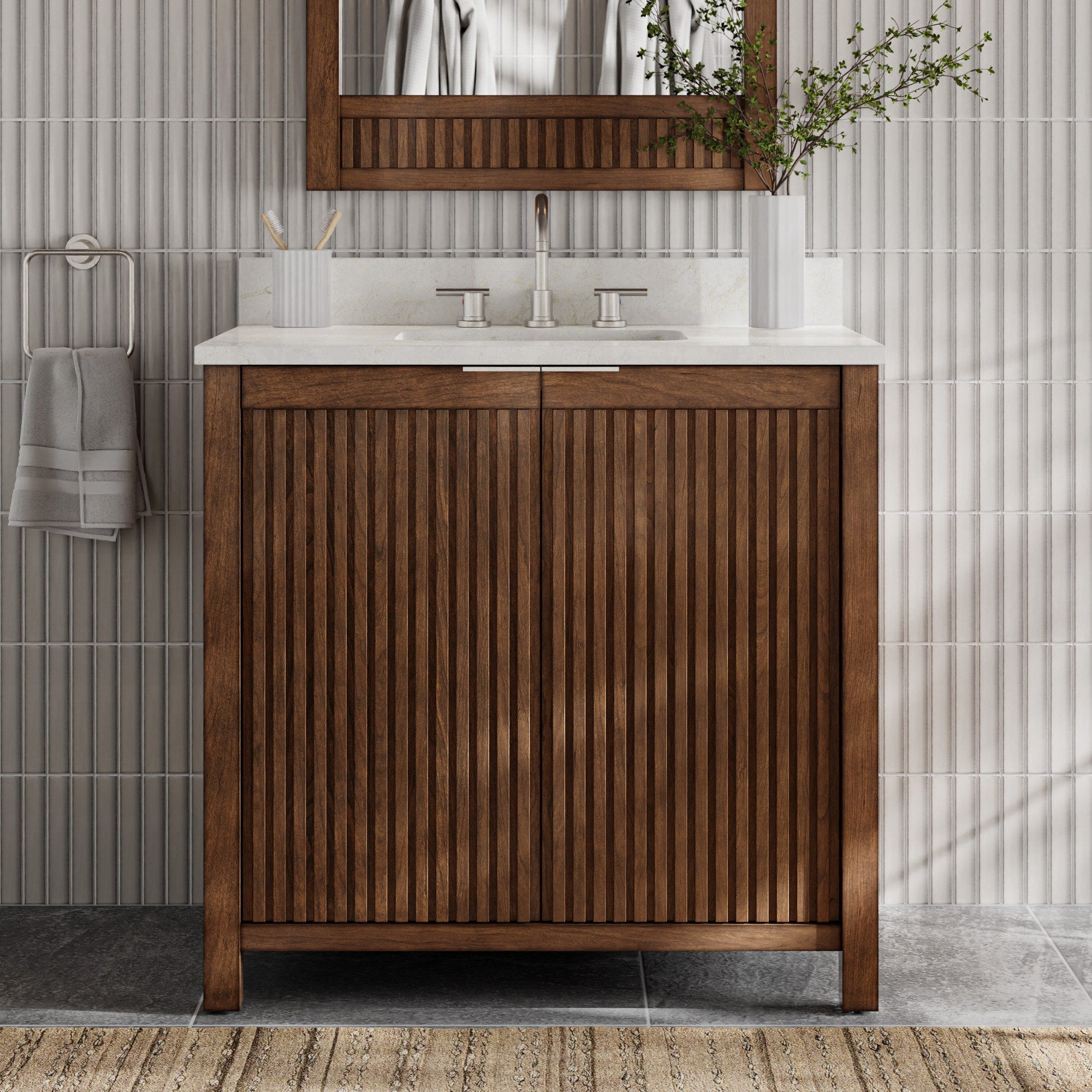 Front view of a modern solid wood single-sink bathroom vanity in warm brown with vertical fluted doors, stone countertop and integrated sink, brushed nickel faucet, wood-framed mirror, towel ring and white vase with greenery.