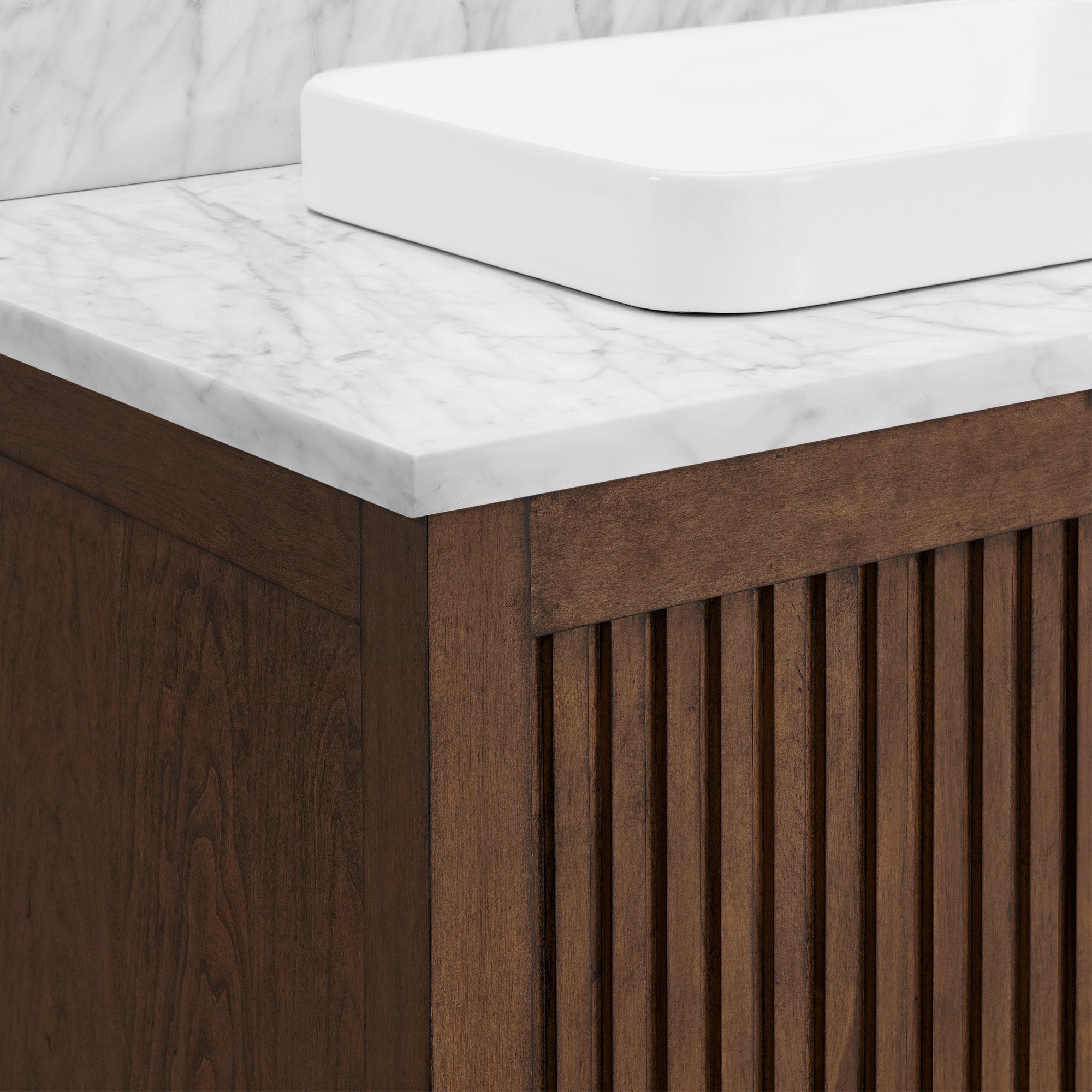 Close-up of a modern solid wood bathroom vanity corner with warm brown fluted cabinet front, white veined stone countertop and a rectangular white ceramic vessel sink.