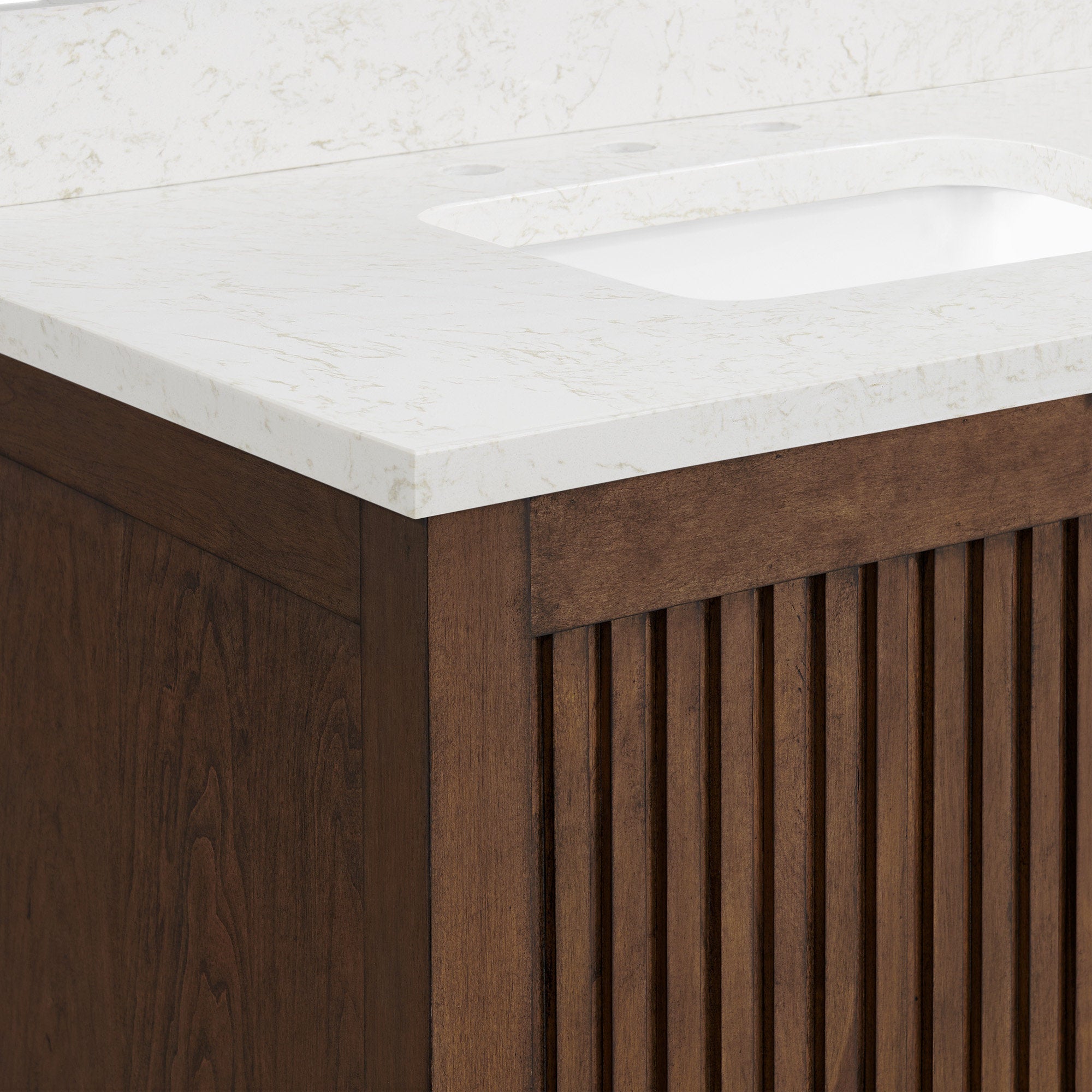 Close-up of a modern single-sink bathroom vanity corner showing a stone-colored white countertop with subtle beige veining, integrated undermount sink and a warm solid wood cabinet with vertical fluted panels.