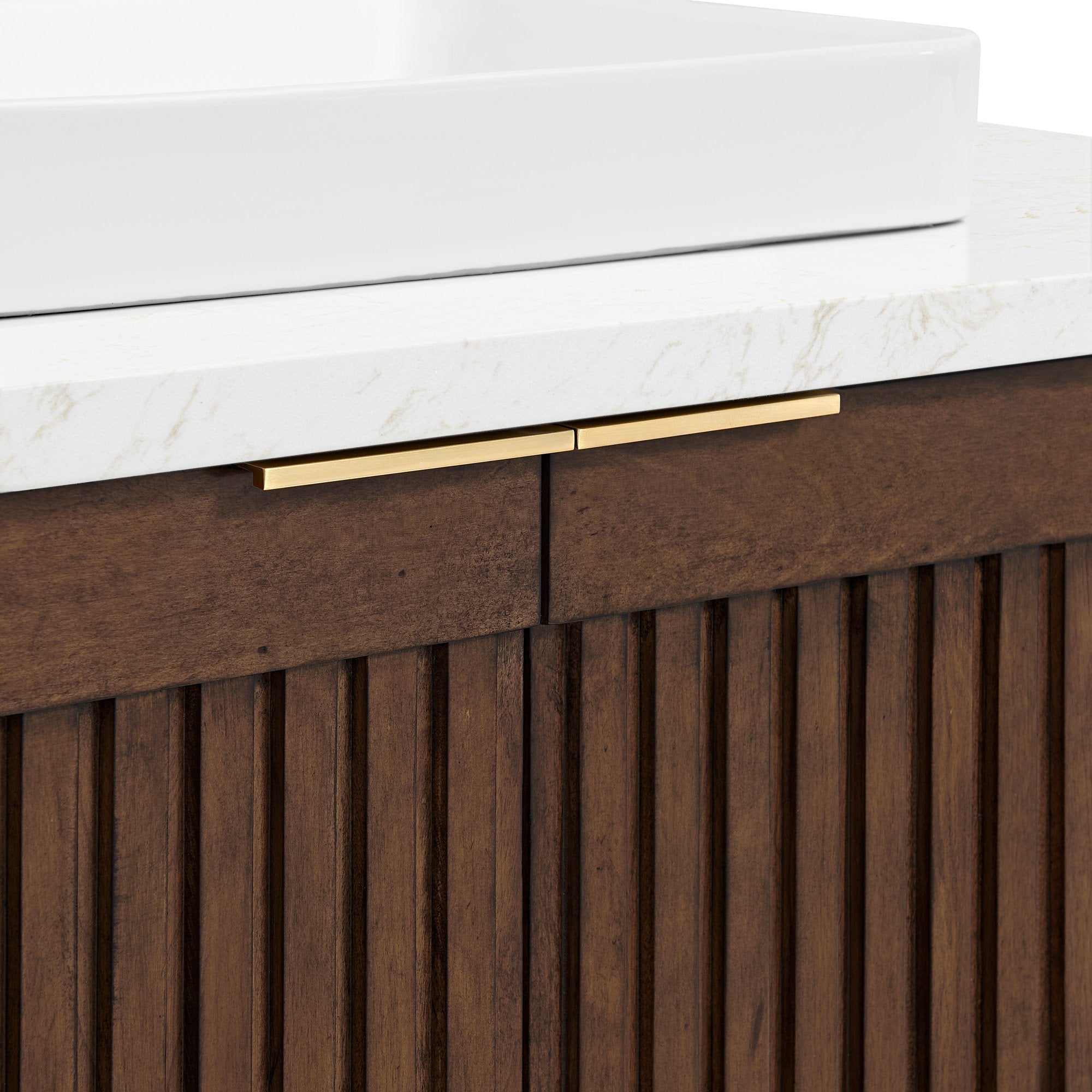 Close-up of a stone countertop with a white ceramic vessel sink sitting above a fluted natural wood vanity in warm brown, accented by slim brass-gold drawer pulls.