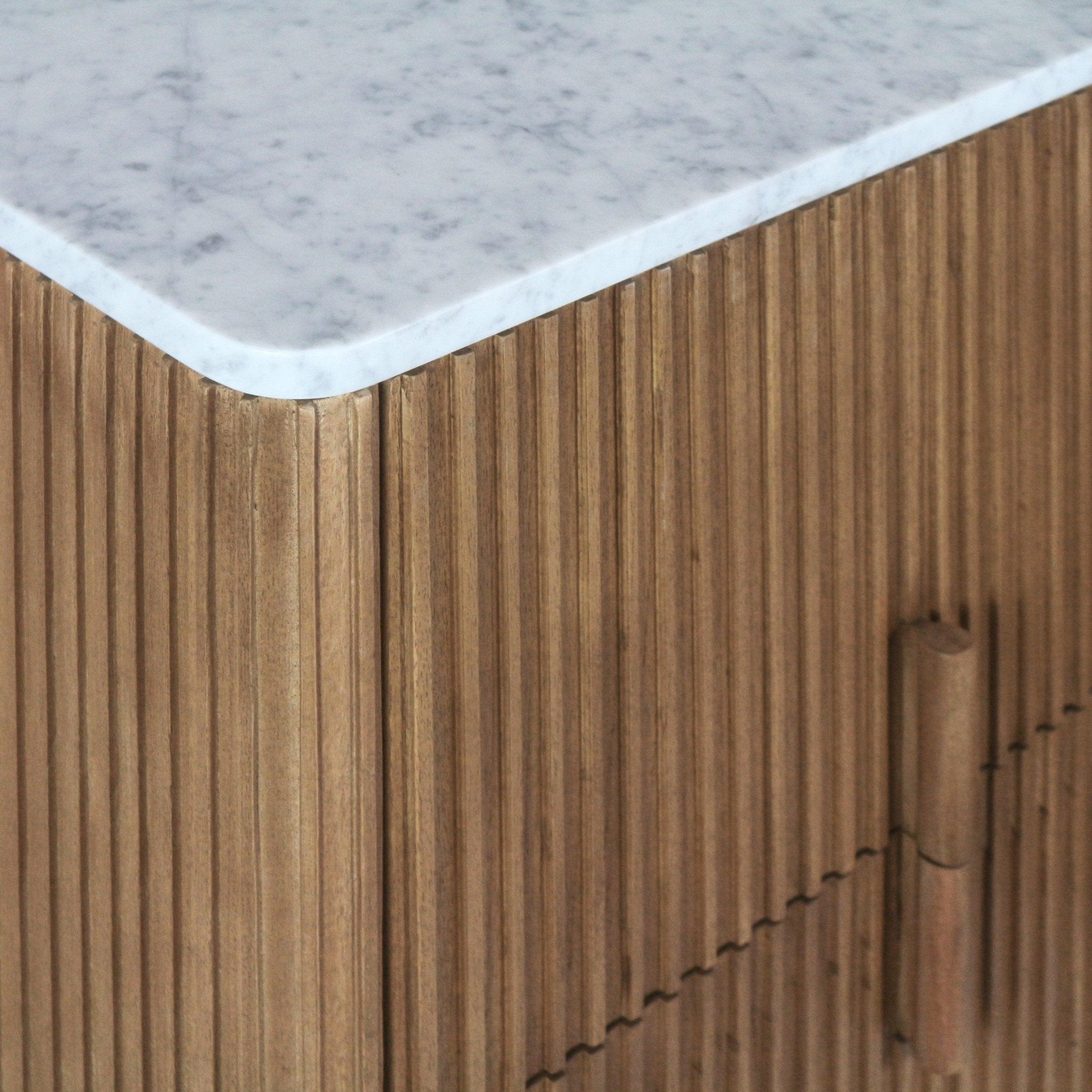 Close-up of a teak sideboard showing vertical fluted wood slats and a rounded white marble top with grey veining, including a cylindrical teak hinge/handle detail on the cabinet front.