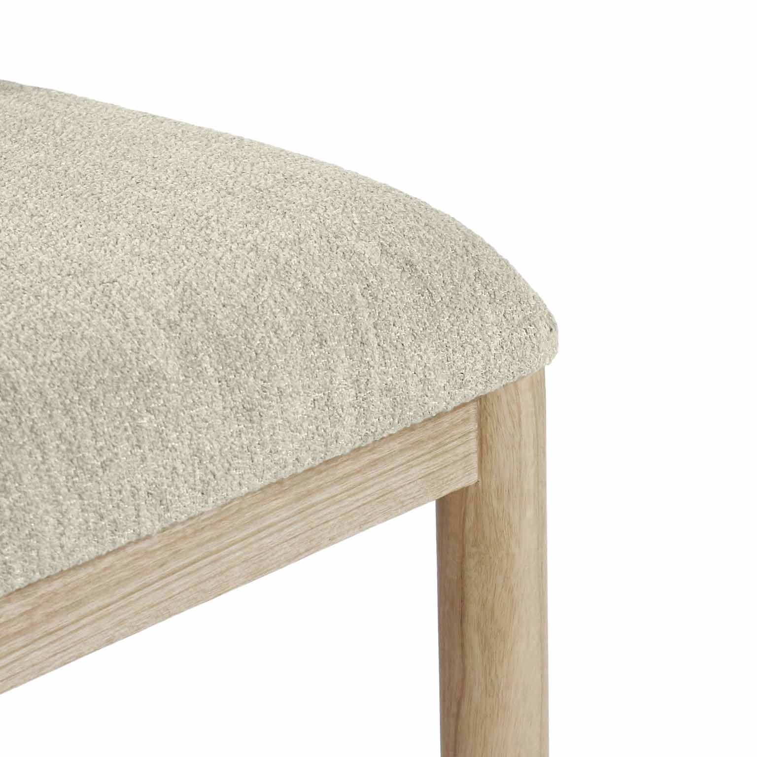 Close-up of a beige bouclé upholstered seat corner atop a natural oak frame and round leg, highlighting the textured fabric and light oak grain.