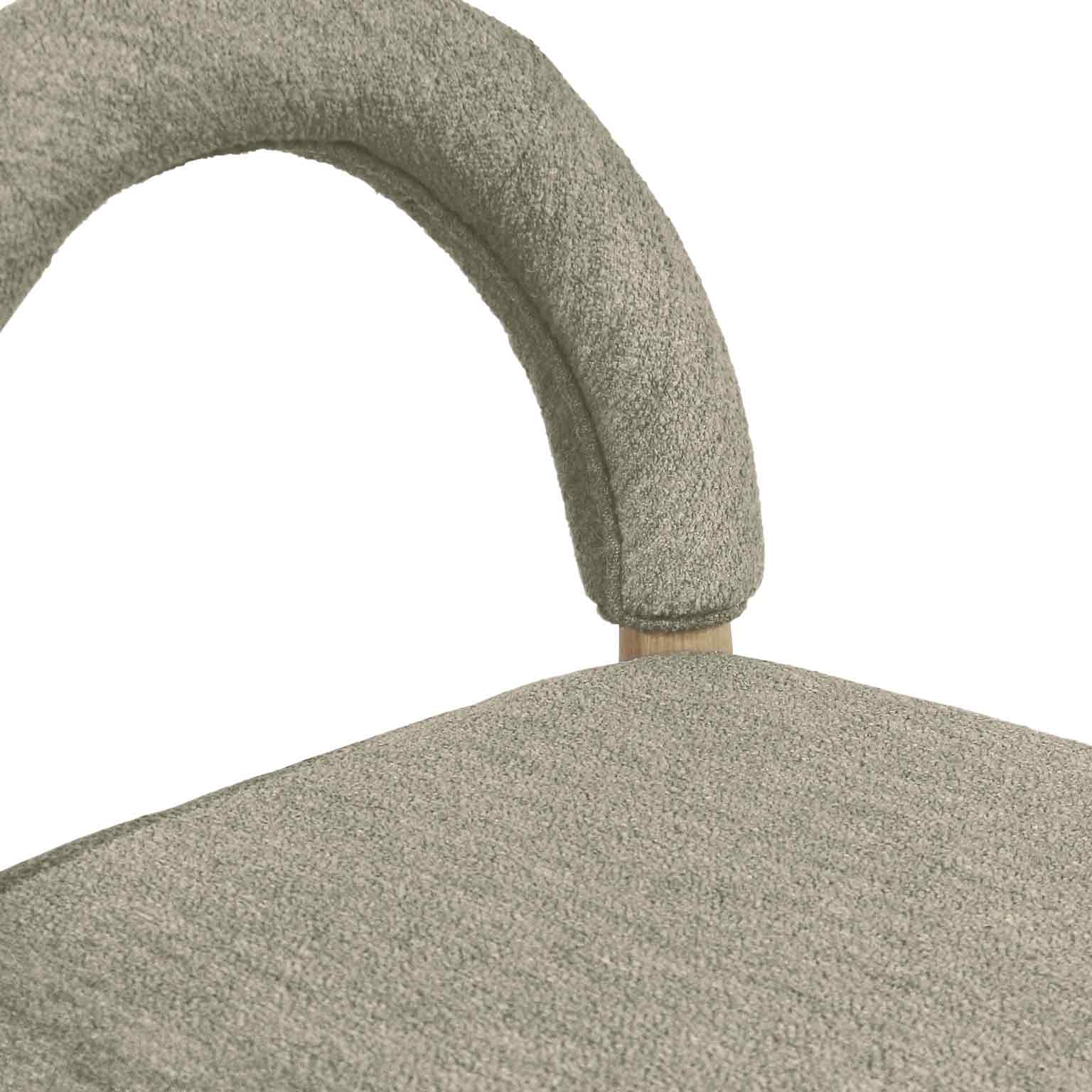 Close-up of taupe boucle upholstery on a counter stool showing the curved arched back, textured seat surface, and a small natural oak connector between back and seat.