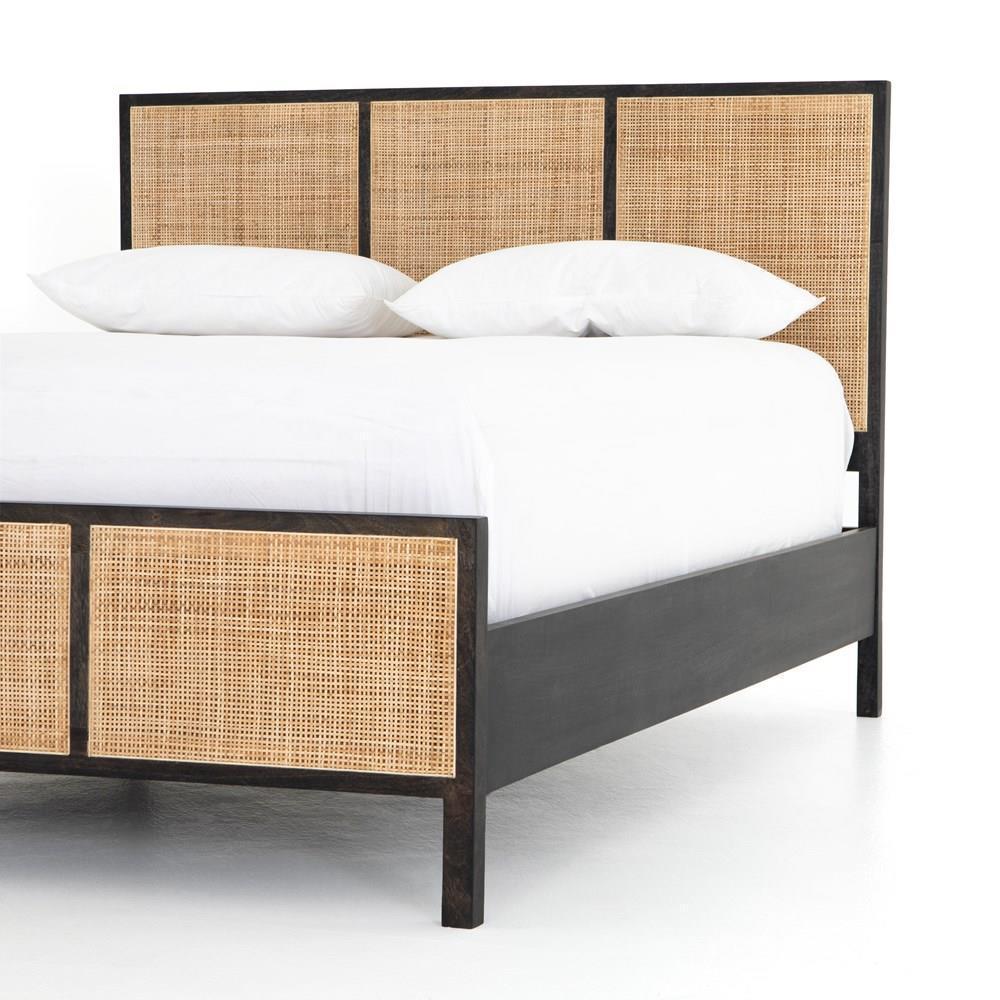 Corner view of a teak platform bed with woven rattan cane panels set in a dark solid wood frame, shown with crisp white bedding and pillows highlighting the boho-style headboard and footboard details.