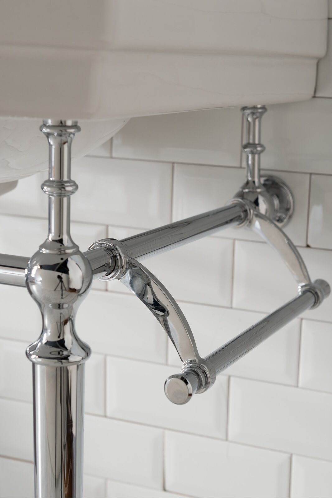 Close-up of polished chrome metal console legs and integrated towel bar supporting a white ceramic sink with a white subway tile backsplash.