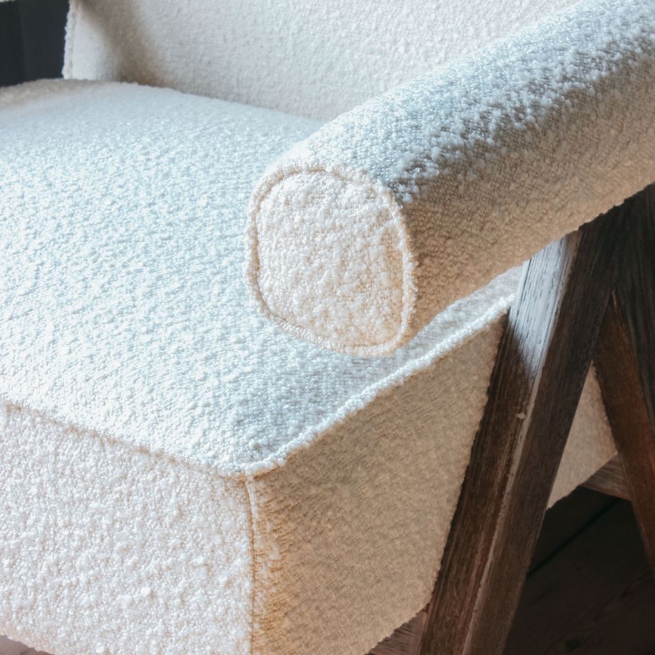 Close-up of a cream boucle-upholstered accent chair showing the textured seat, rounded arm bolster, and exposed natural wood frame leg.