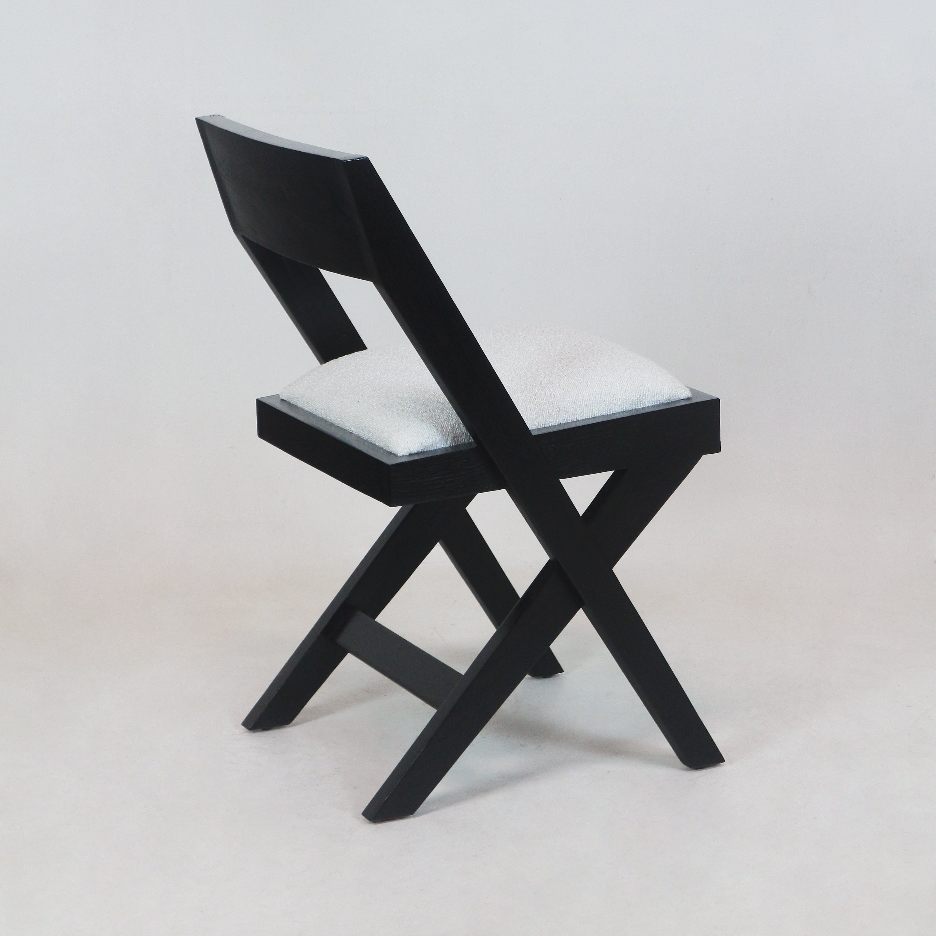 Armless black wood side chair with crossed X-shaped legs and a white upholstered boucle seat cushion, shown at a three-quarter angle on a neutral background.