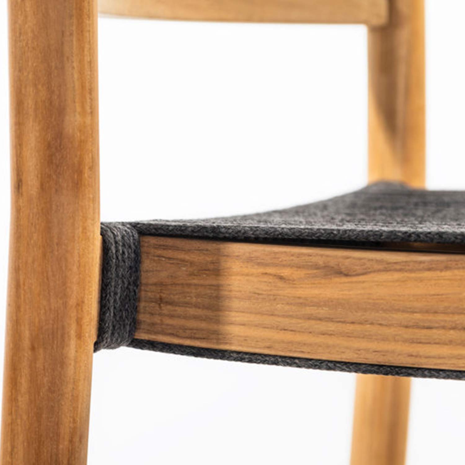 Close-up of a teak bar stool seat edge showing natural wood grain, gray upholstered fabric top and a braided gray rope wrap securing the seat to the vertical teak leg.