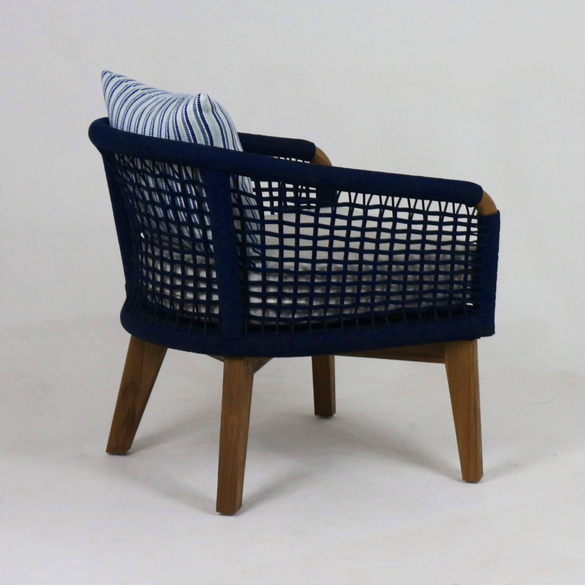 Modern outdoor lounge chair with natural wood legs, navy UV-protected rope weave on the back and sides, a cushioned fabric seat and a white-and-navy striped throw pillow.