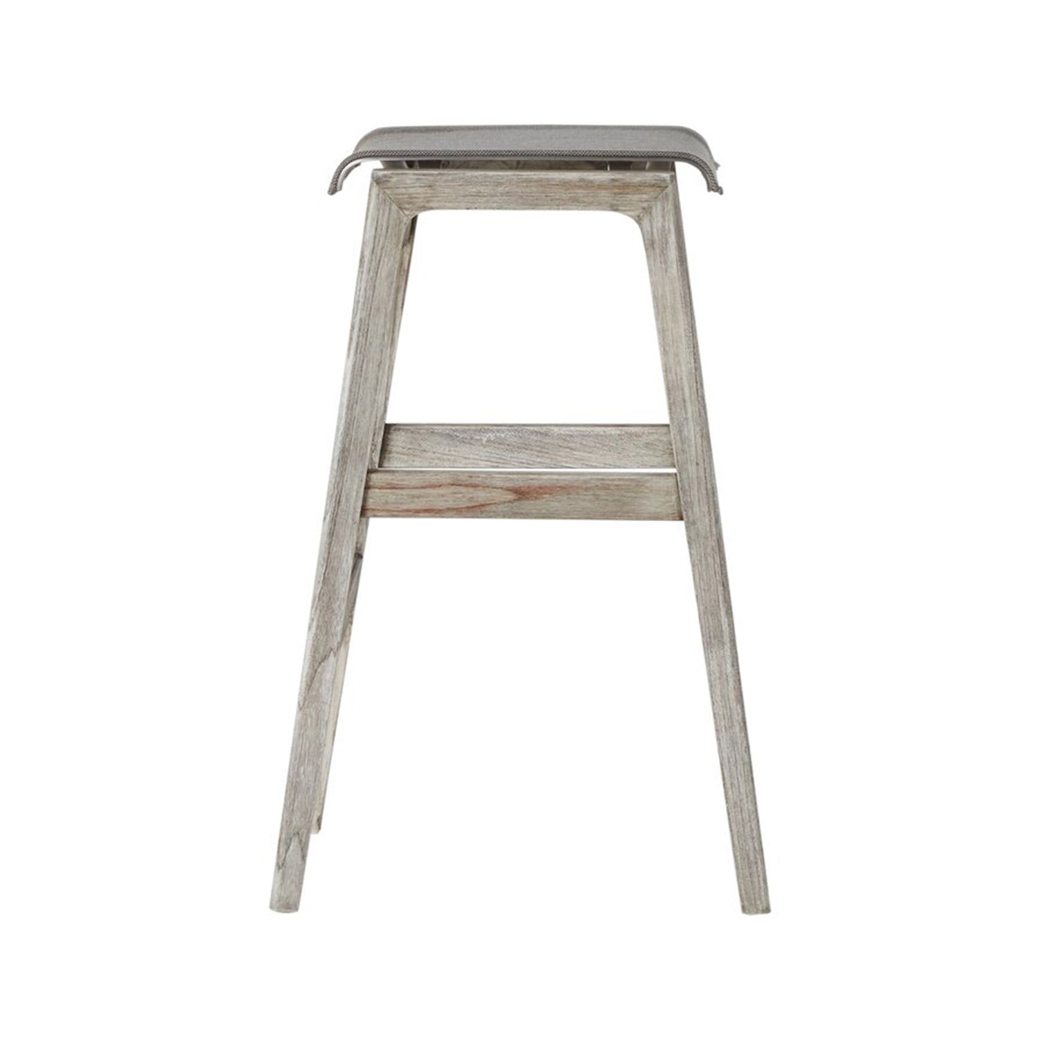 Back view of a backless outdoor bar stool in natural teak with a gray canvas seat, tapered legs and a horizontal footrest slat showing weathered wood grain in a coastal-modern style.