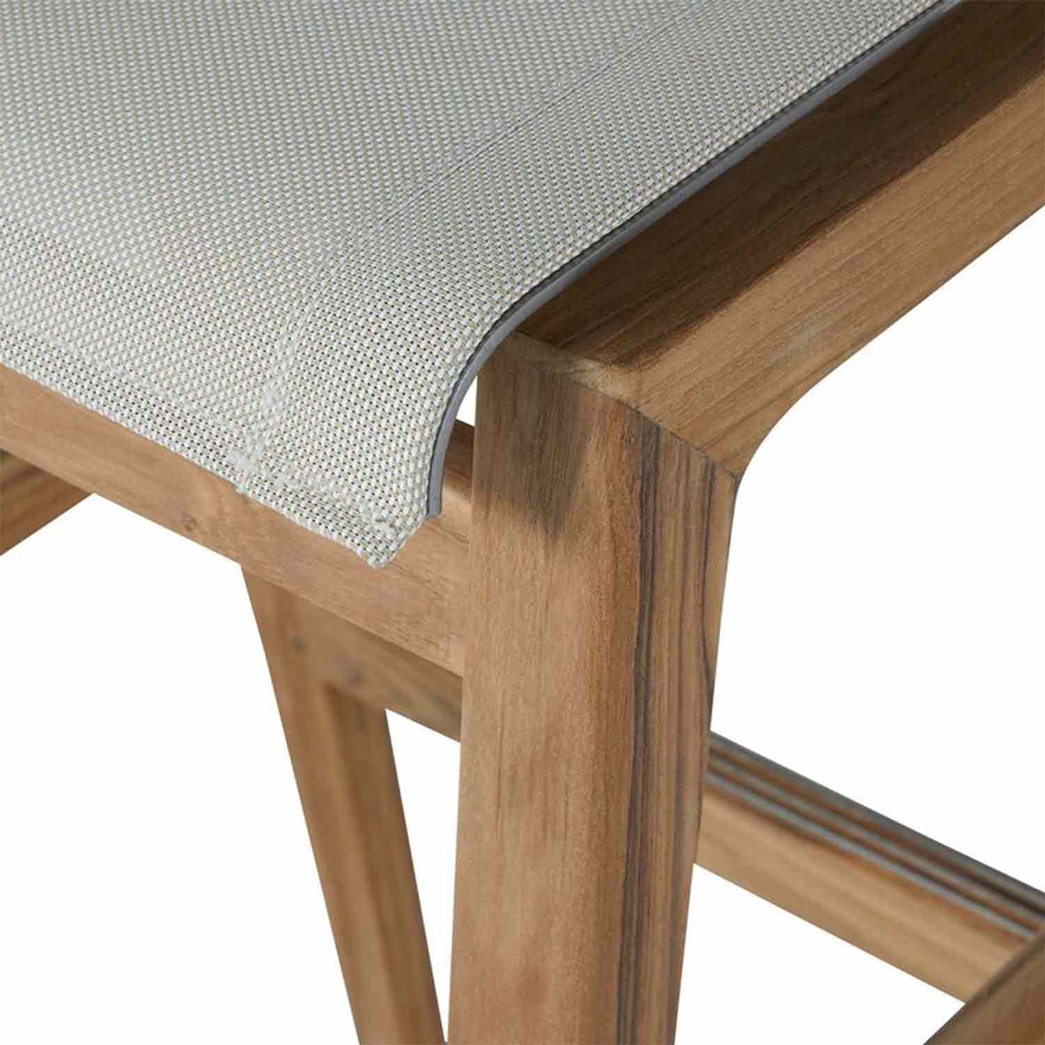 Close-up of a backless teak outdoor bar stool showing natural teak wood frame with visible grain and a light natural canvas seat corner with stitched edge and curved joint.