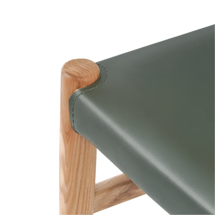 Close-up of an olive green faux leather seat corner with visible stitching wrapped around a natural ash wood leg and rounded top cap, showing materials and join detail of the armless side chair.