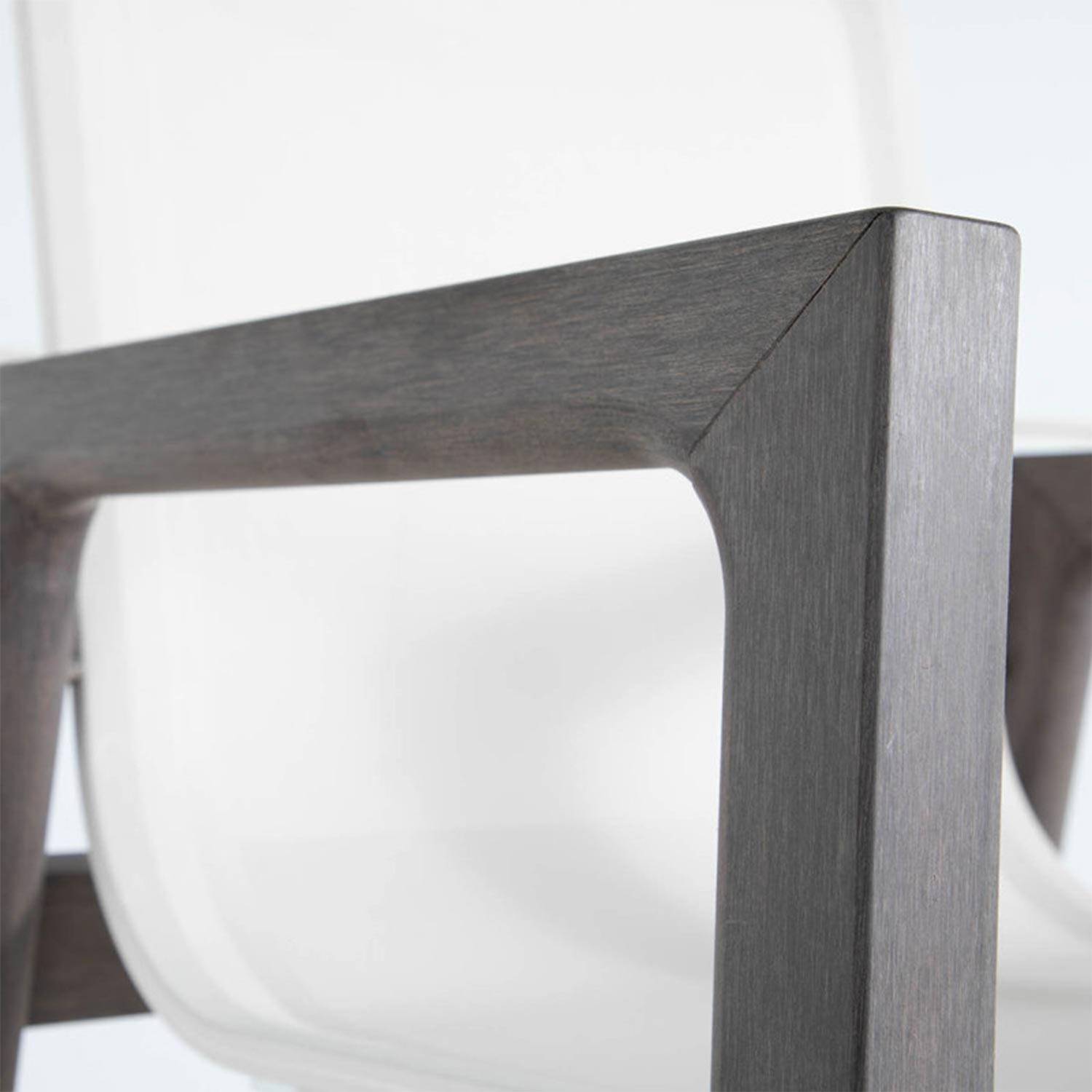 Close-up of a teak armrest and corner joint on an outdoor bar stool, showing warm natural teak wood grain with a curved white molded seat visible in the background.