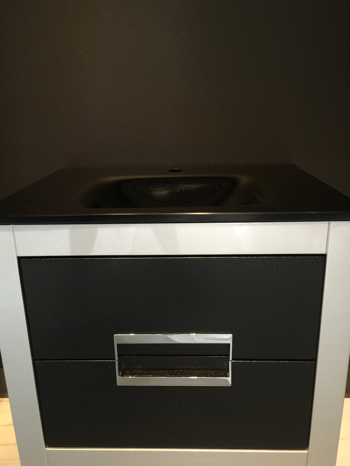 Front view of a modern single-sink bathroom vanity with a black stone integrated top and basin, white wooden frame, textured black drawer fronts and a rectangular chrome drawer pull.
