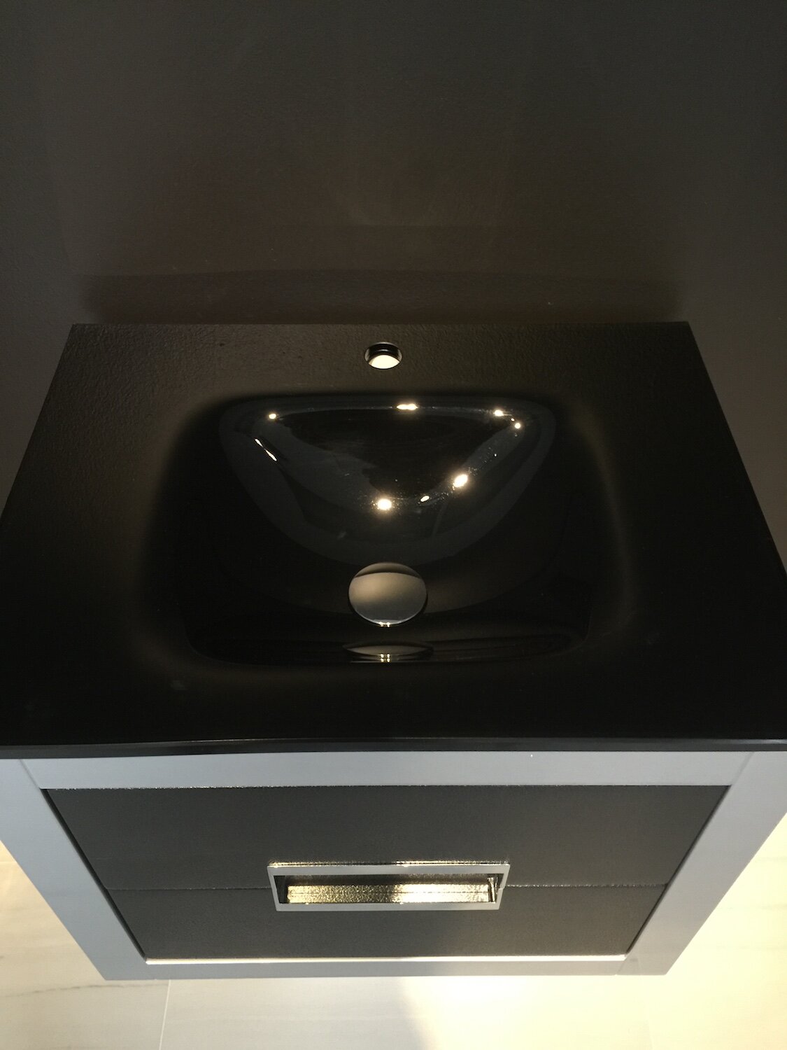 Top-down view of a modern solid wood bathroom vanity with a stone-colored top and glossy black ceramic sink, single faucet hole and chrome rectangular drawer pull.