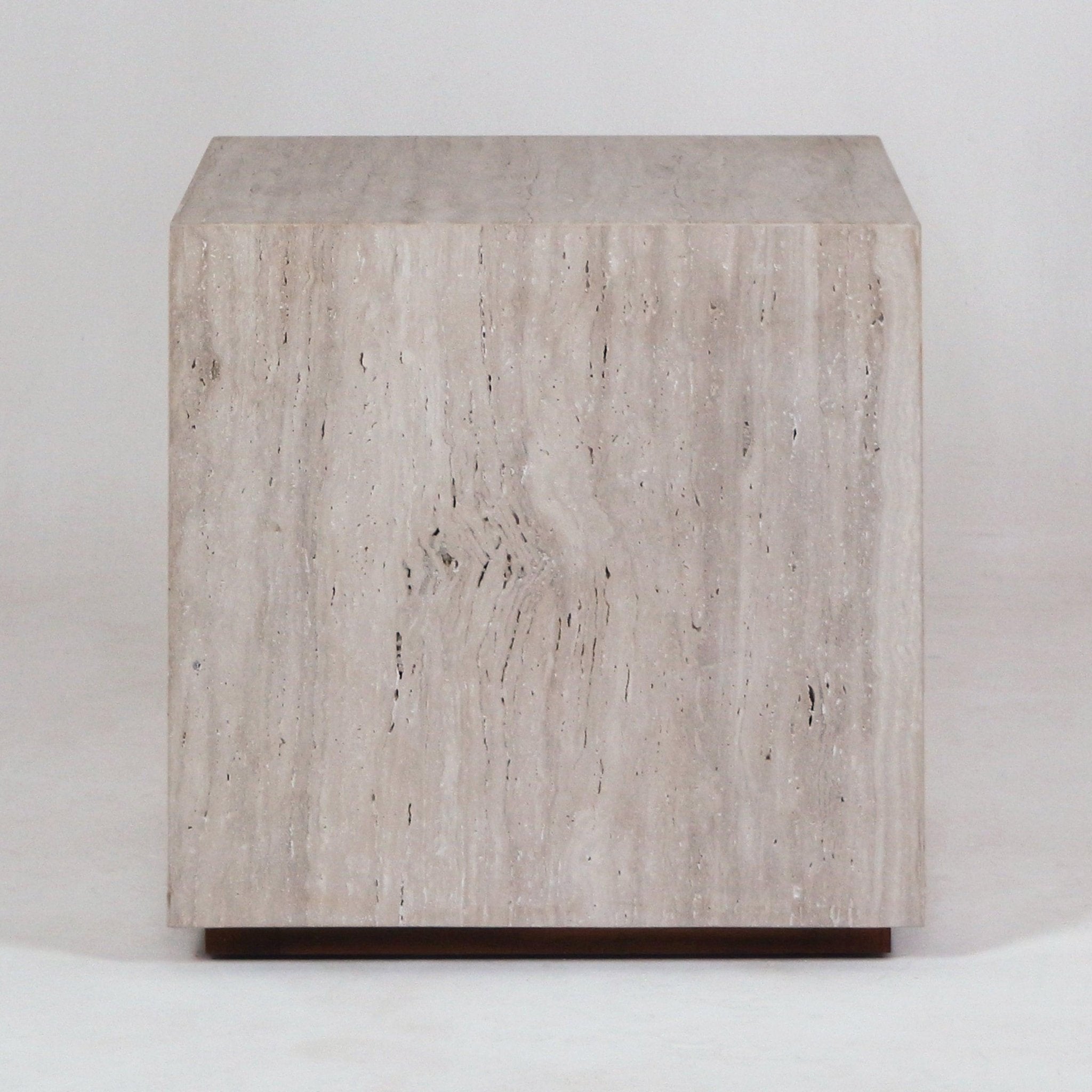 Front view of a modern cube-shaped nightstand made from natural beige travertine with subtle vertical veining, sitting on a slim wood base.