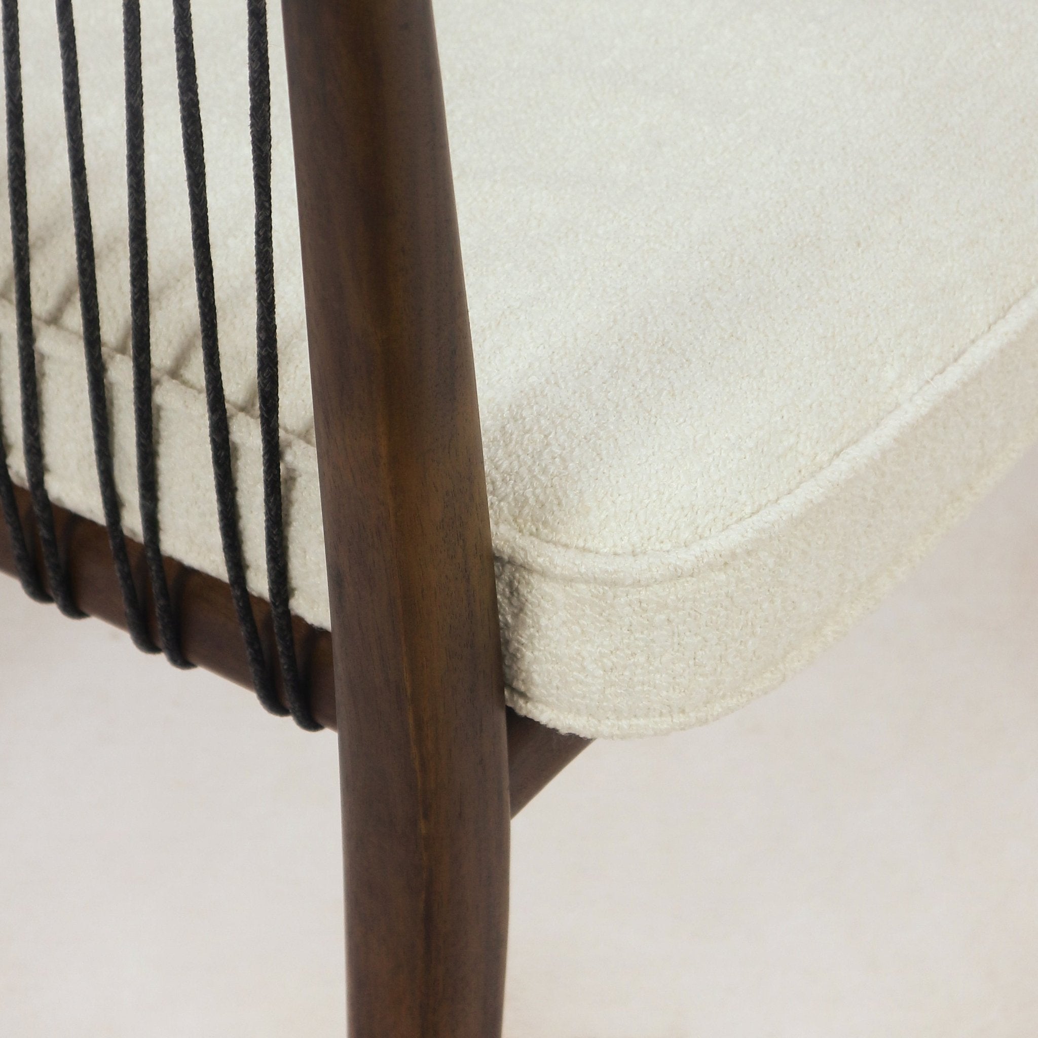 Close-up of a cream boucle upholstered seat cushion with piped edge on a mahogany-finished solid wood frame and vertical black rope back detail.