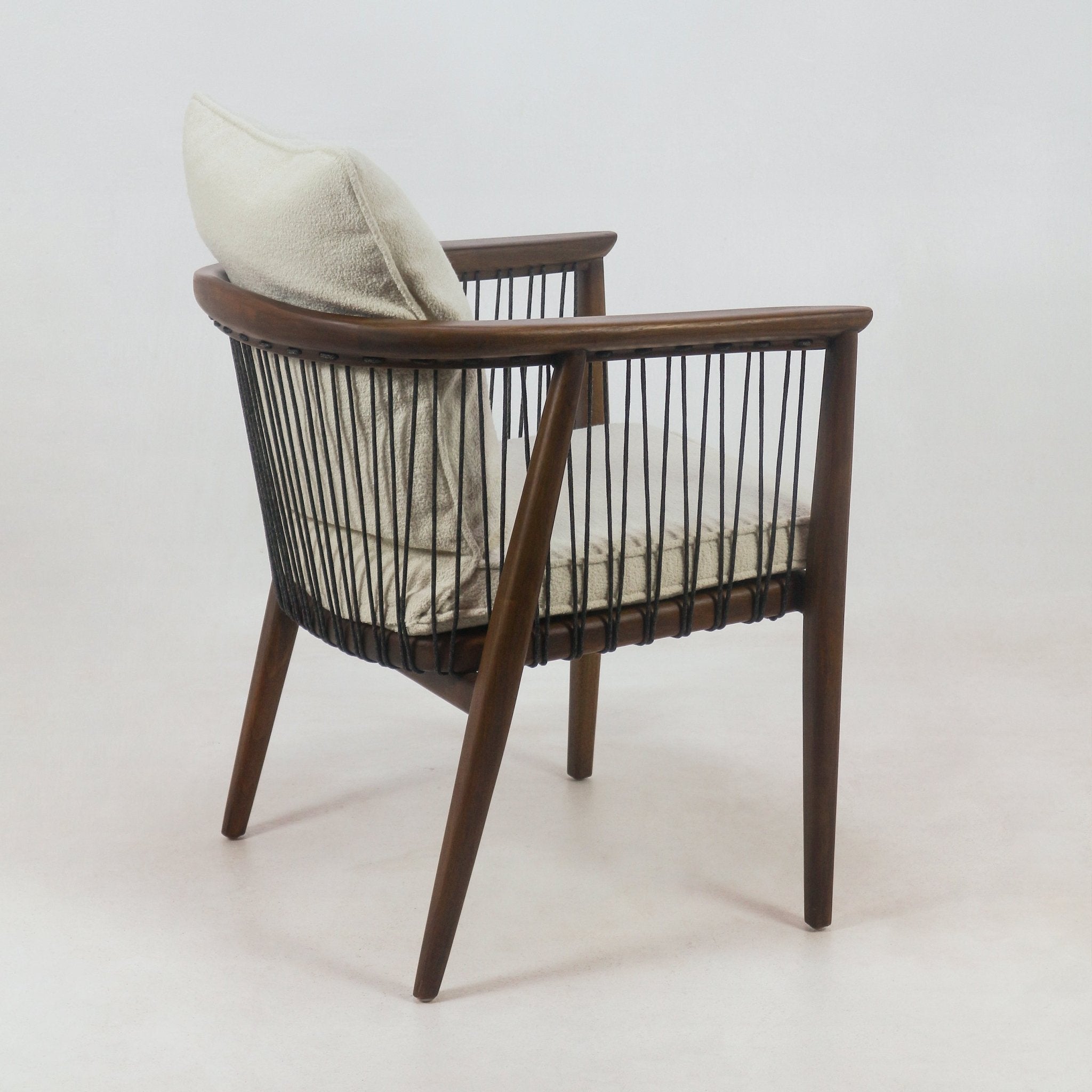 Solid wood dining chair in a mahogany finish with cream boucle seat and back cushions, black rope-spindle sides, curved wooden arms and tapered legs, shown from a rear three-quarter view.