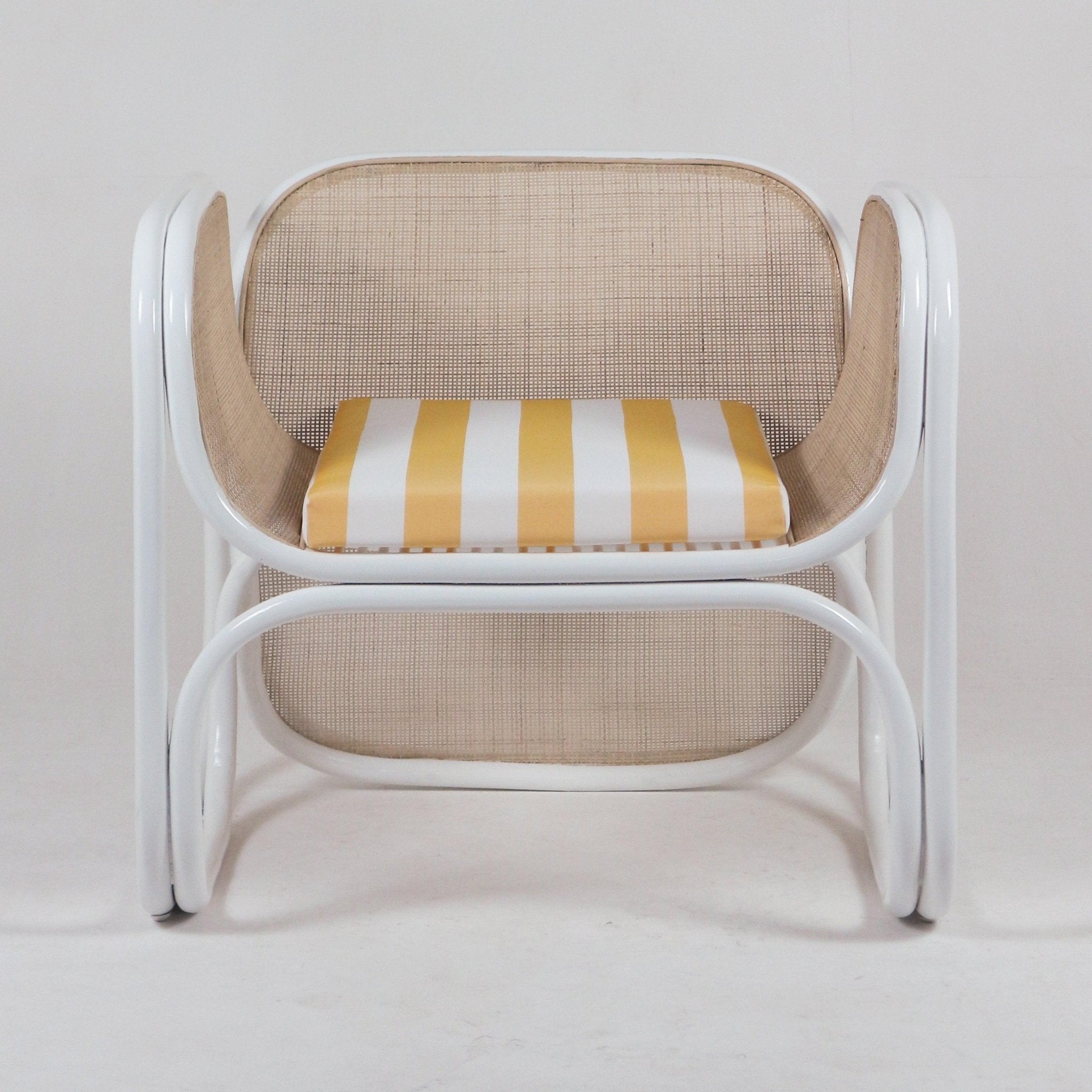 Modern lounge chair with a curved white tubular frame, natural woven cane back and sides, and a yellow-and-white striped fabric seat cushion.