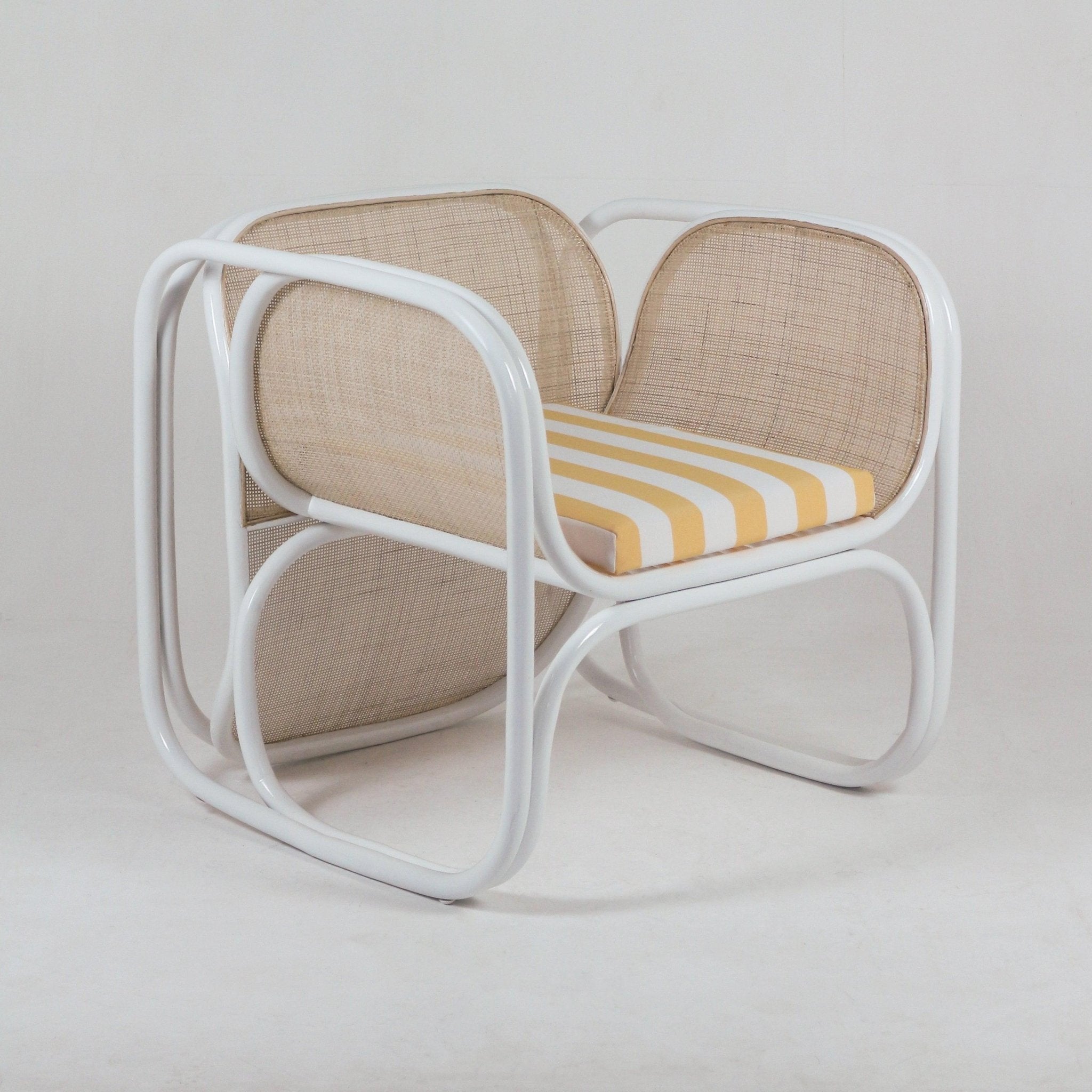 Modern lounge chair with a white metal frame, natural cane back and sides, and a yellow-and-white striped fabric seat cushion shown on a neutral studio background.