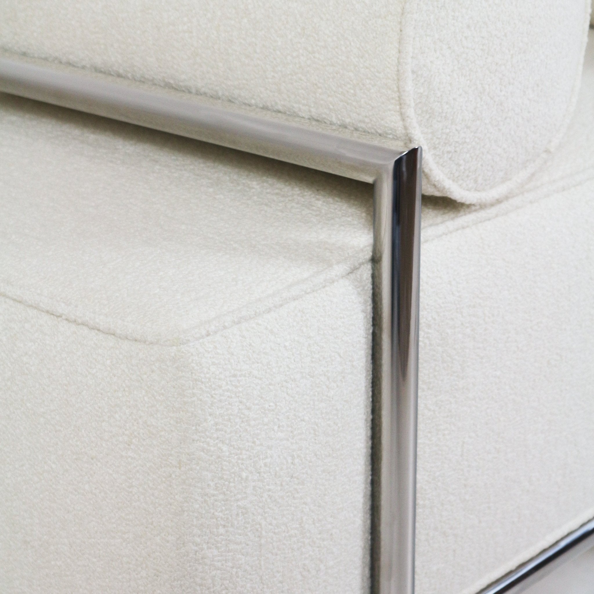 Close-up of a cream boucle upholstered bench seat with a rounded bolster and polished metal frame, highlighting fabric texture, seam detail, and modern end-of-bed bench styling.