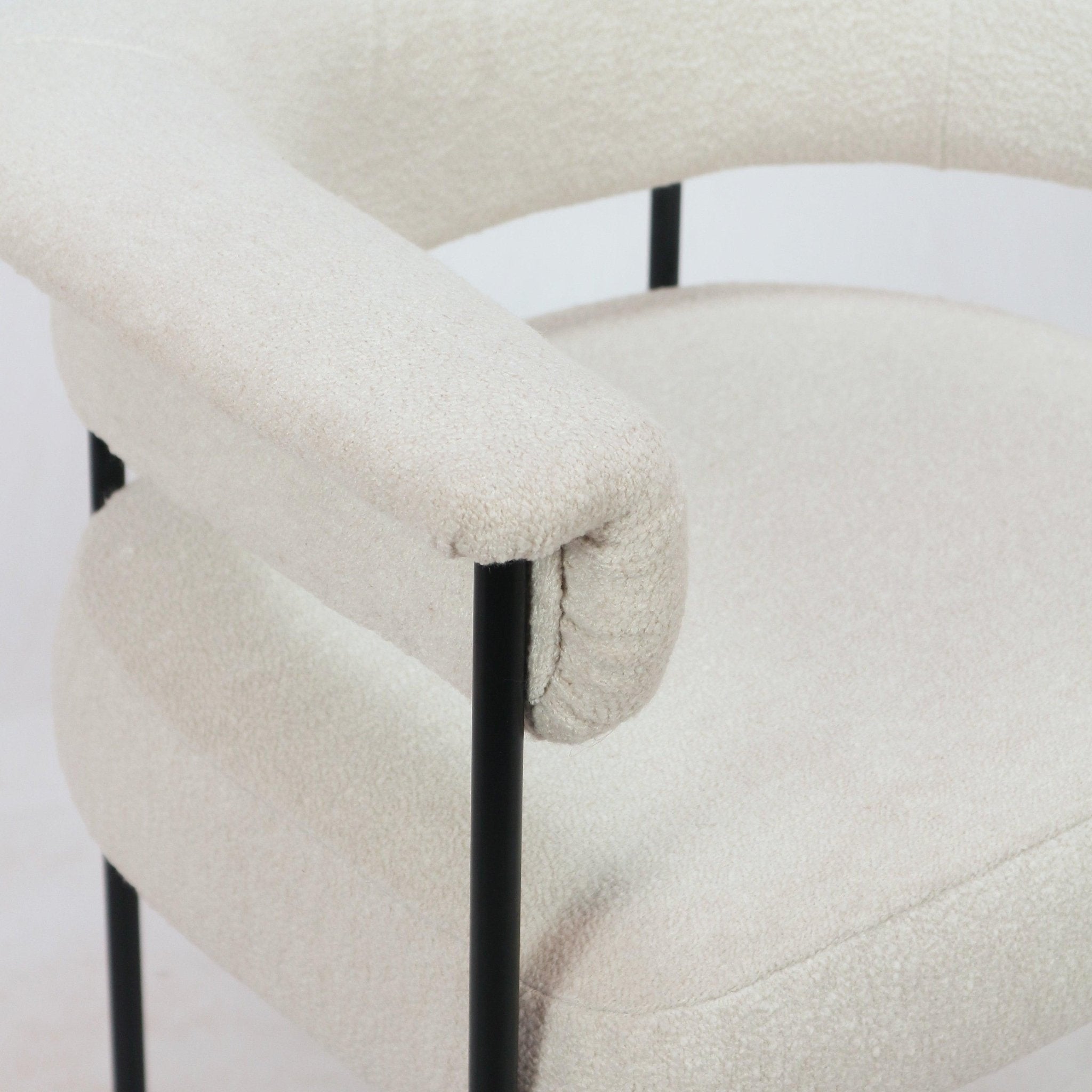 Close-up of a cream boucle upholstered counter stool showing the rounded cushioned seat, curved low backrest and slim black metal frame supports.