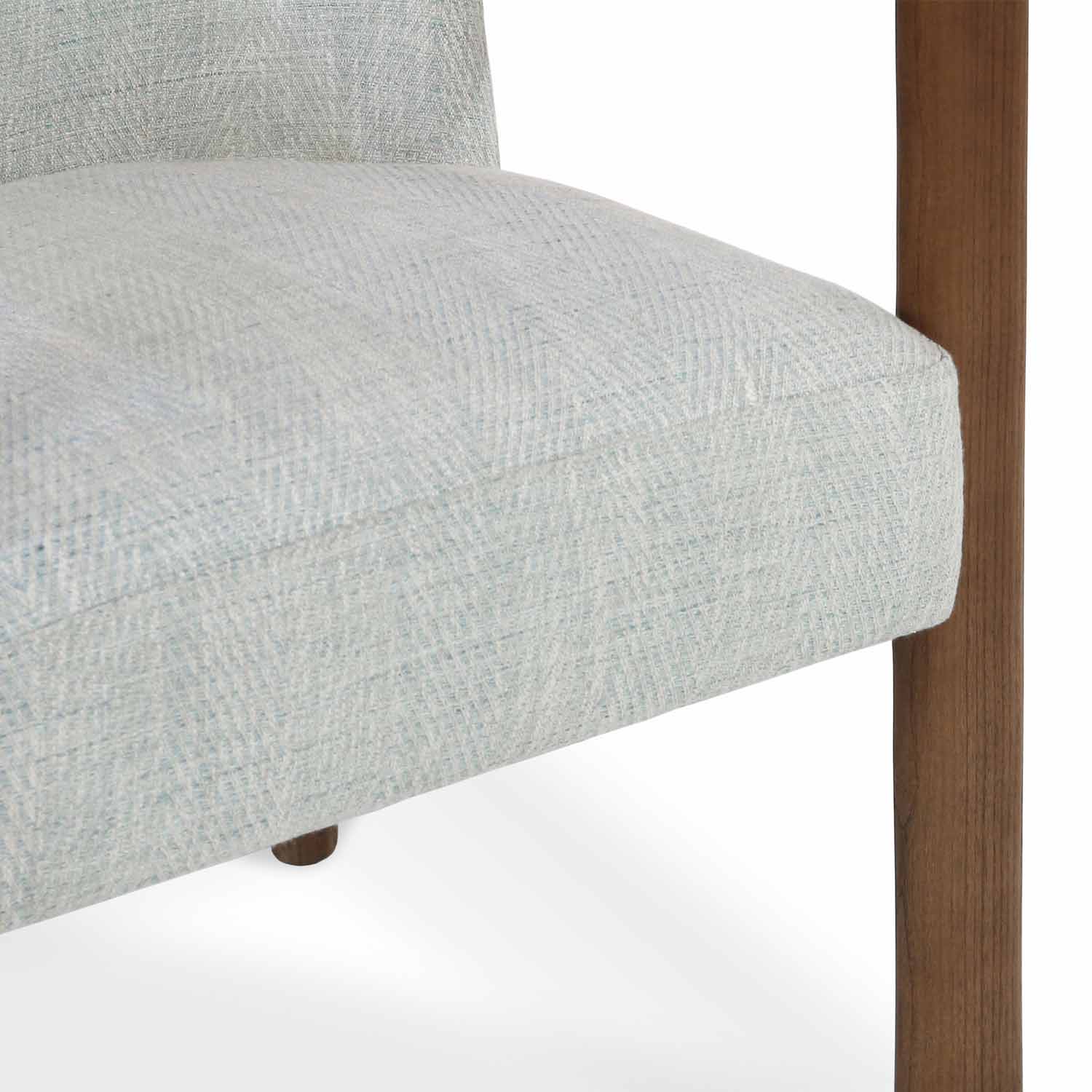 Close-up of a light gray herringbone polyester-upholstered dining chair seat and padded back, showing a warm oak wood leg and small tapered wooden foot.