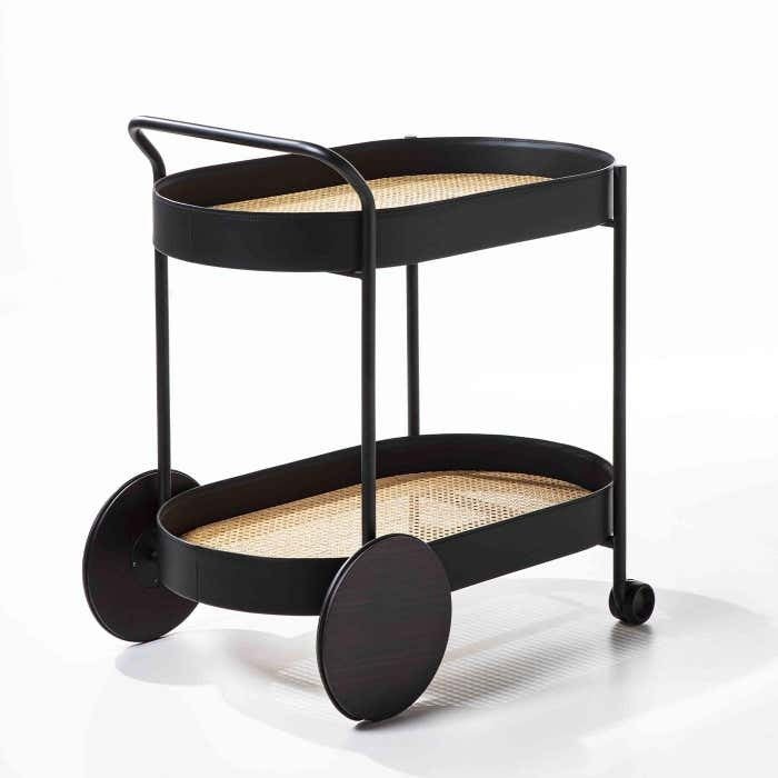 Modern two-tier bar cart with a matte black metal frame, woven rattan (cane) shelves, oversized round rear wheels and small front casters, shown on a white background.