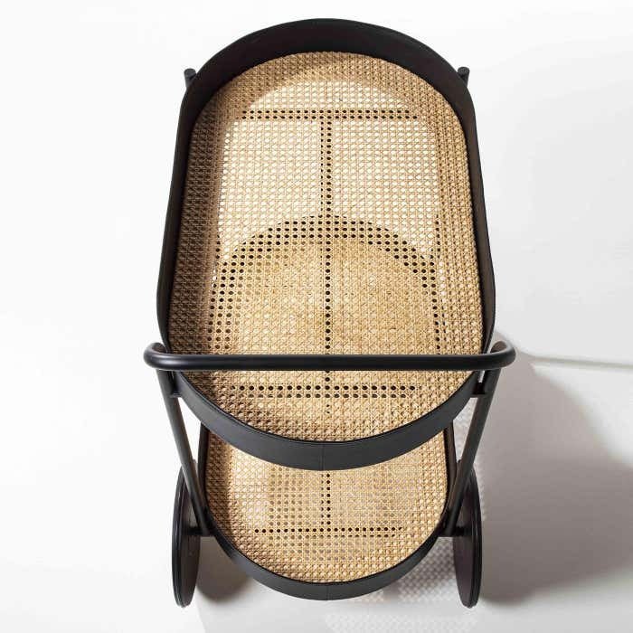 Top-down view of a modern matte black metal two-tier bar cart with woven natural rattan cane shelves and oversized black wheels.
