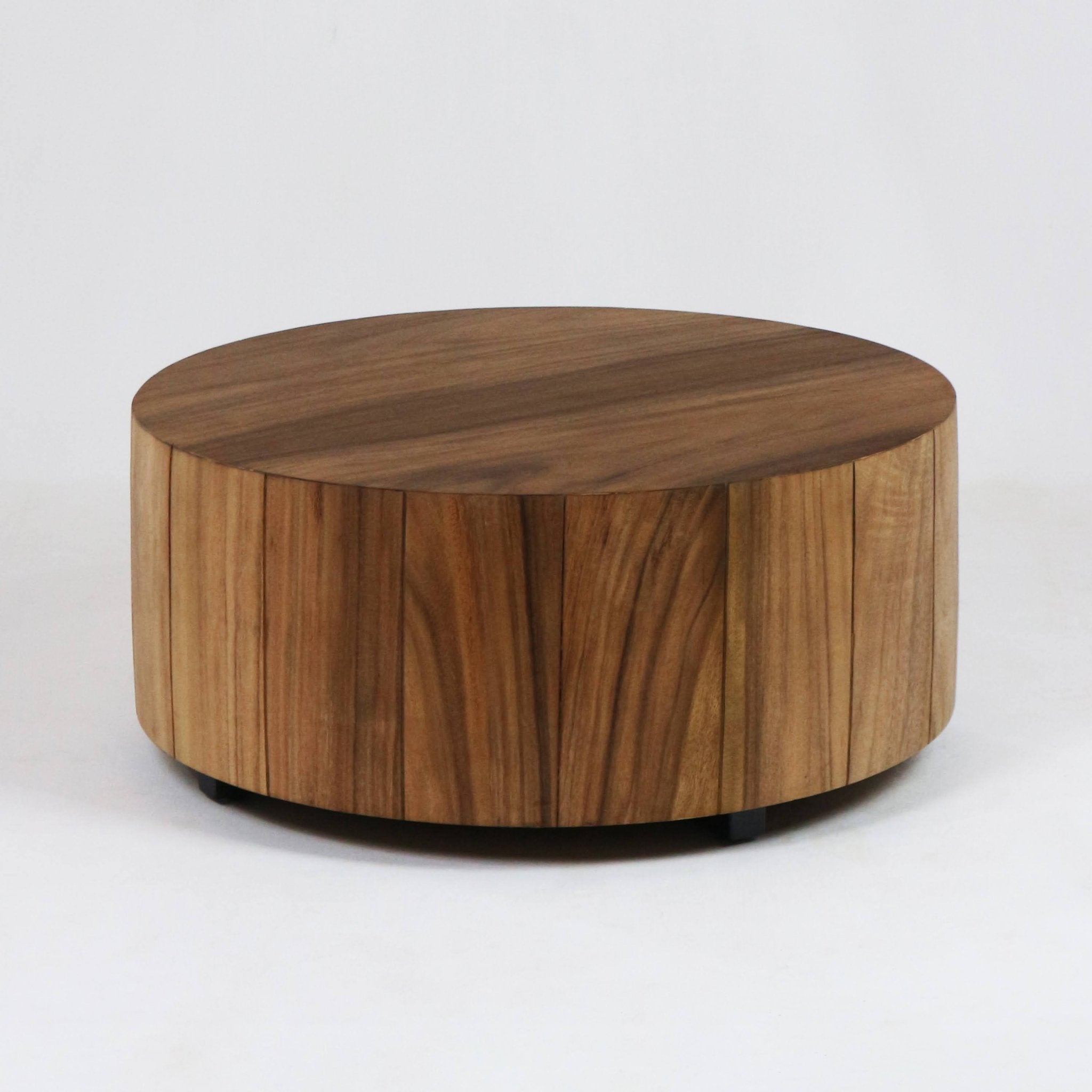 Low, round solid wood coffee table with a warm natural wood finish, vertical plank sides, smooth circular top and low black feet, shown on a white background — modern, minimalist design for the living room.