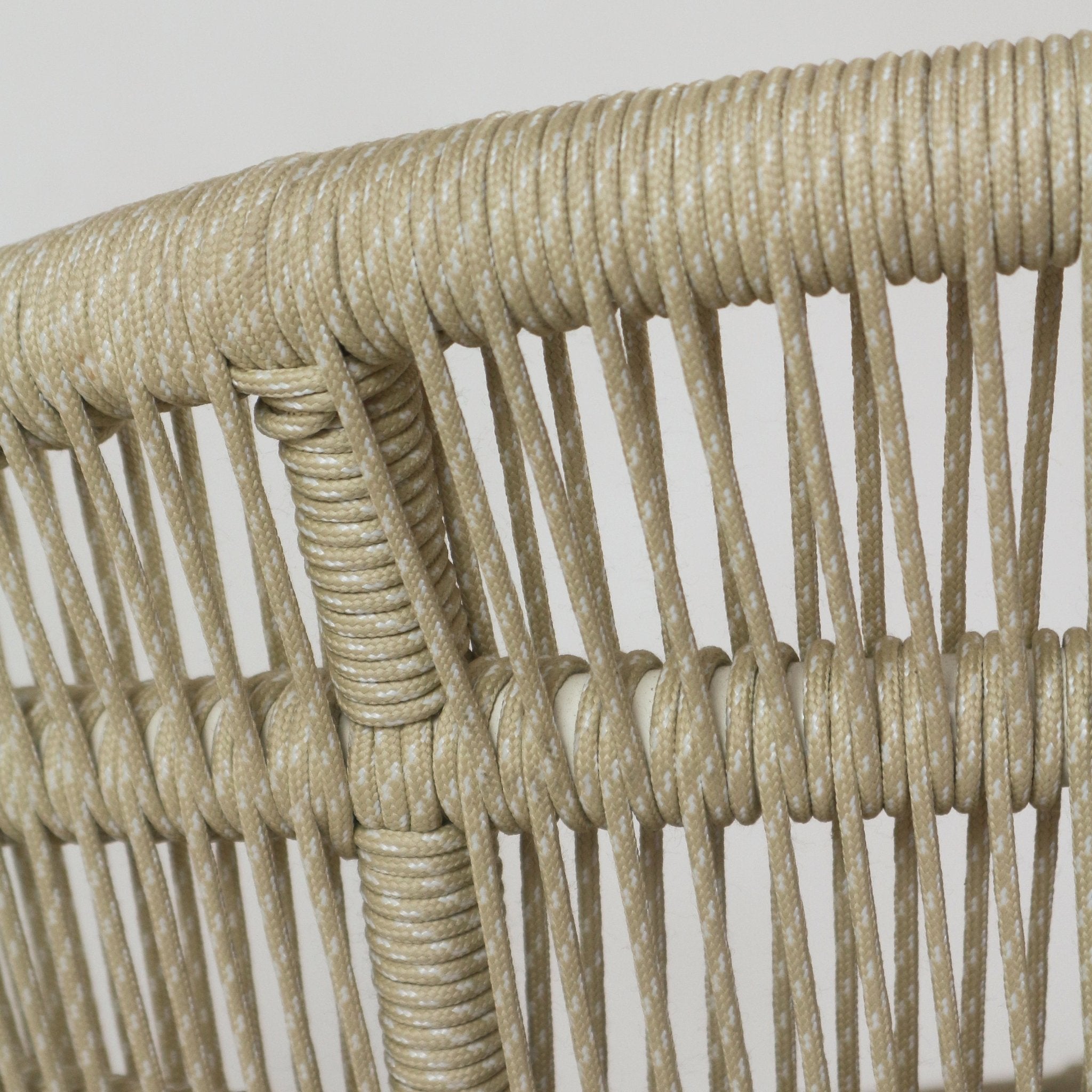 Close-up of beige outdoor rope with white fleck tightly wrapped and woven around a metal chair frame, showing vertical cord detailing and knotted intersections on a coastal-style patio chair back.