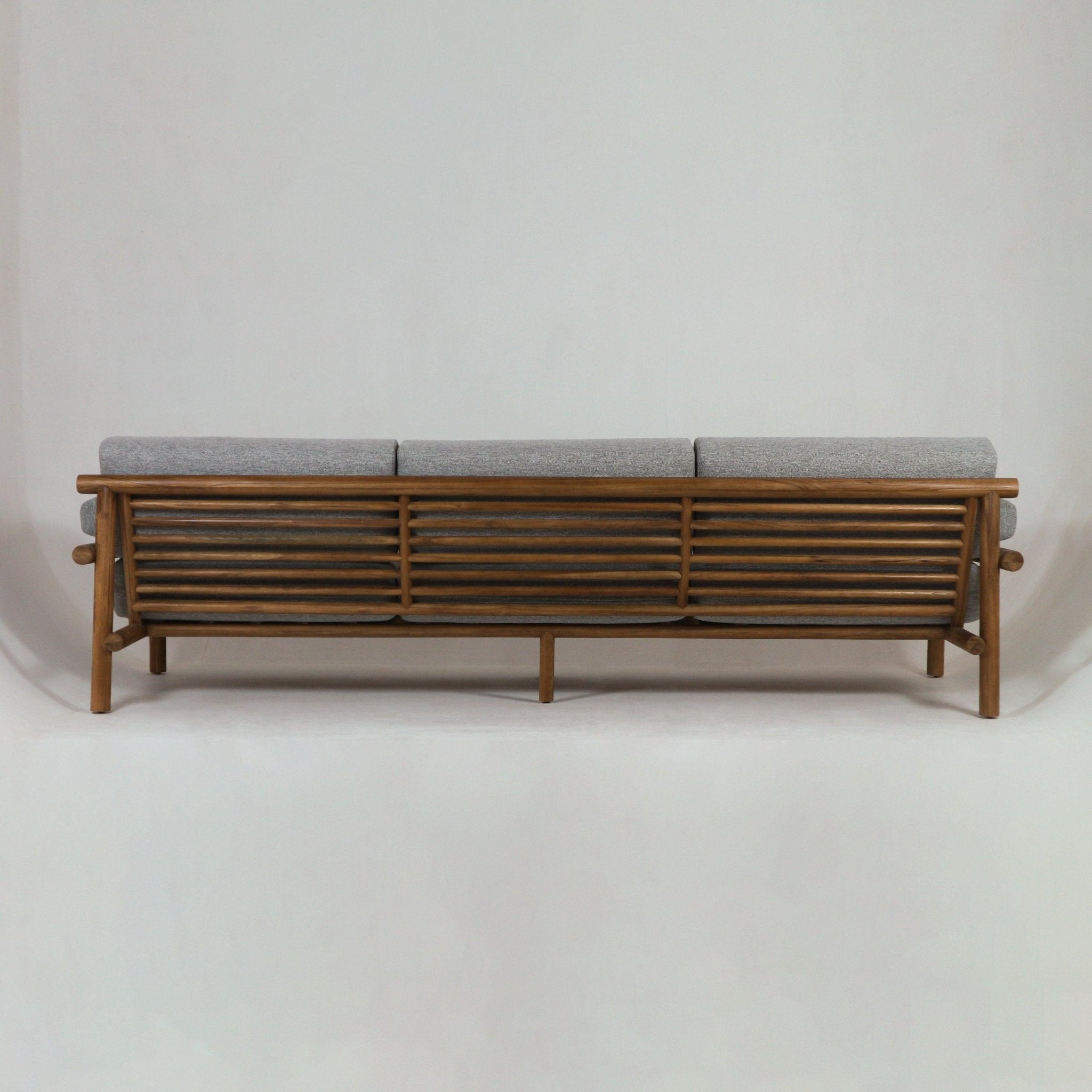 Rear view of an outdoor teak sofa showing a horizontal slatted teak frame and three gray Sunbrella fabric seat and back cushions, coastal-modern styling against a neutral studio background.