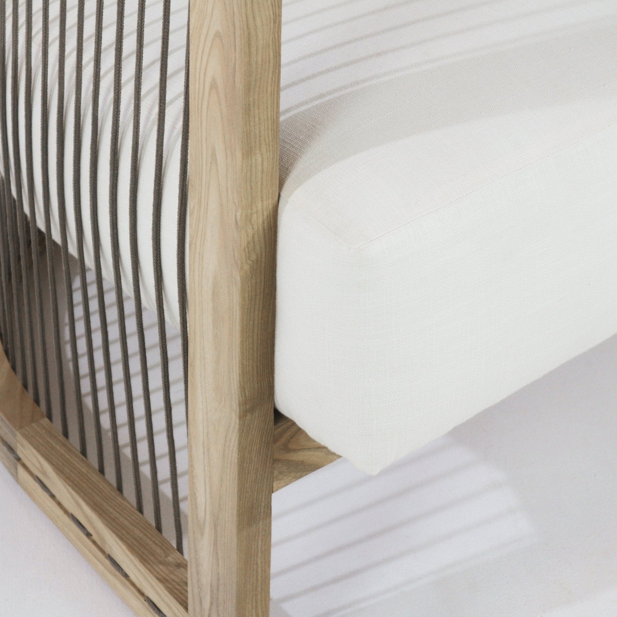 Close-up of a dining chair's natural wood frame with vertical gray rope back and an off-white fabric seat cushion, highlighting the wood grain and the tailored cushion corner in a contemporary Scandinavian style.