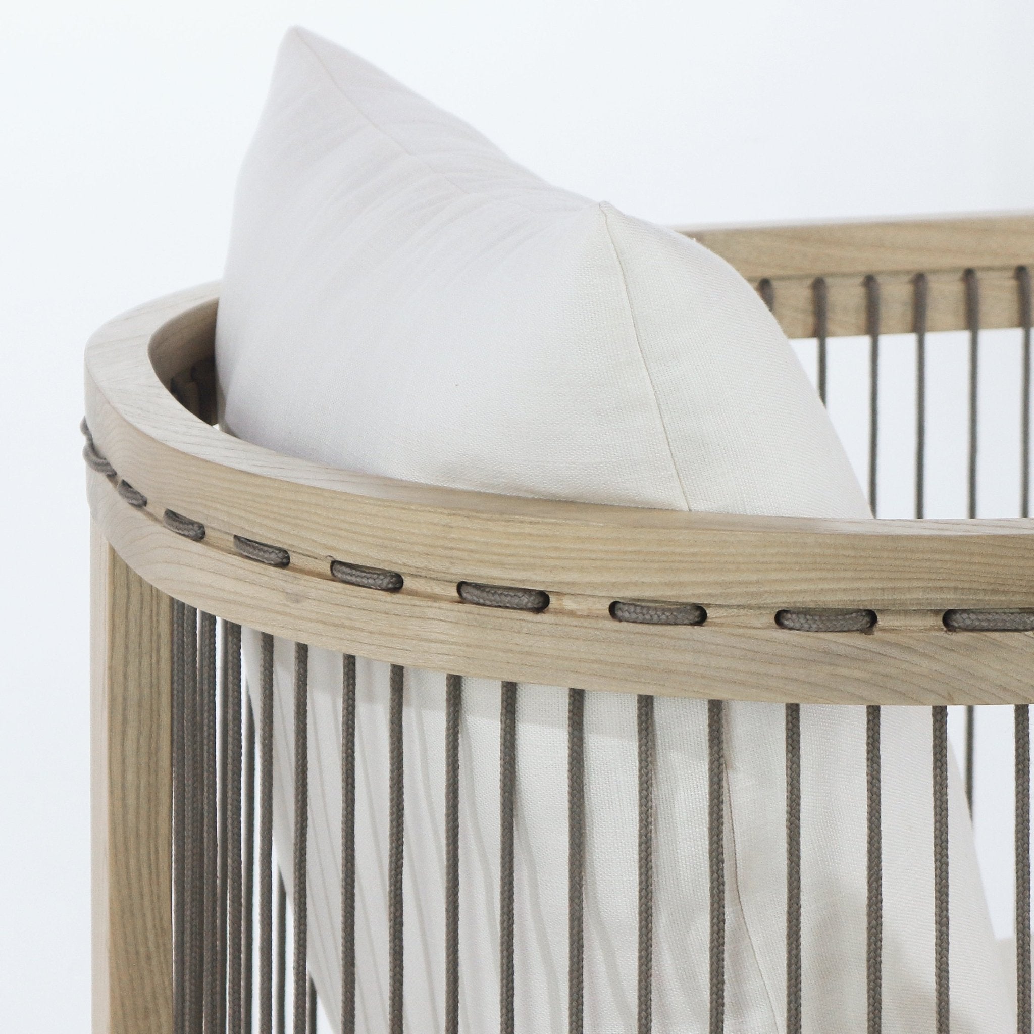 Close-up of a dining chair back with a curved natural oak top rail, taupe rope lacing and vertical rope cords, and a cream fabric cushion nestled inside the modern Scandinavian-style frame.