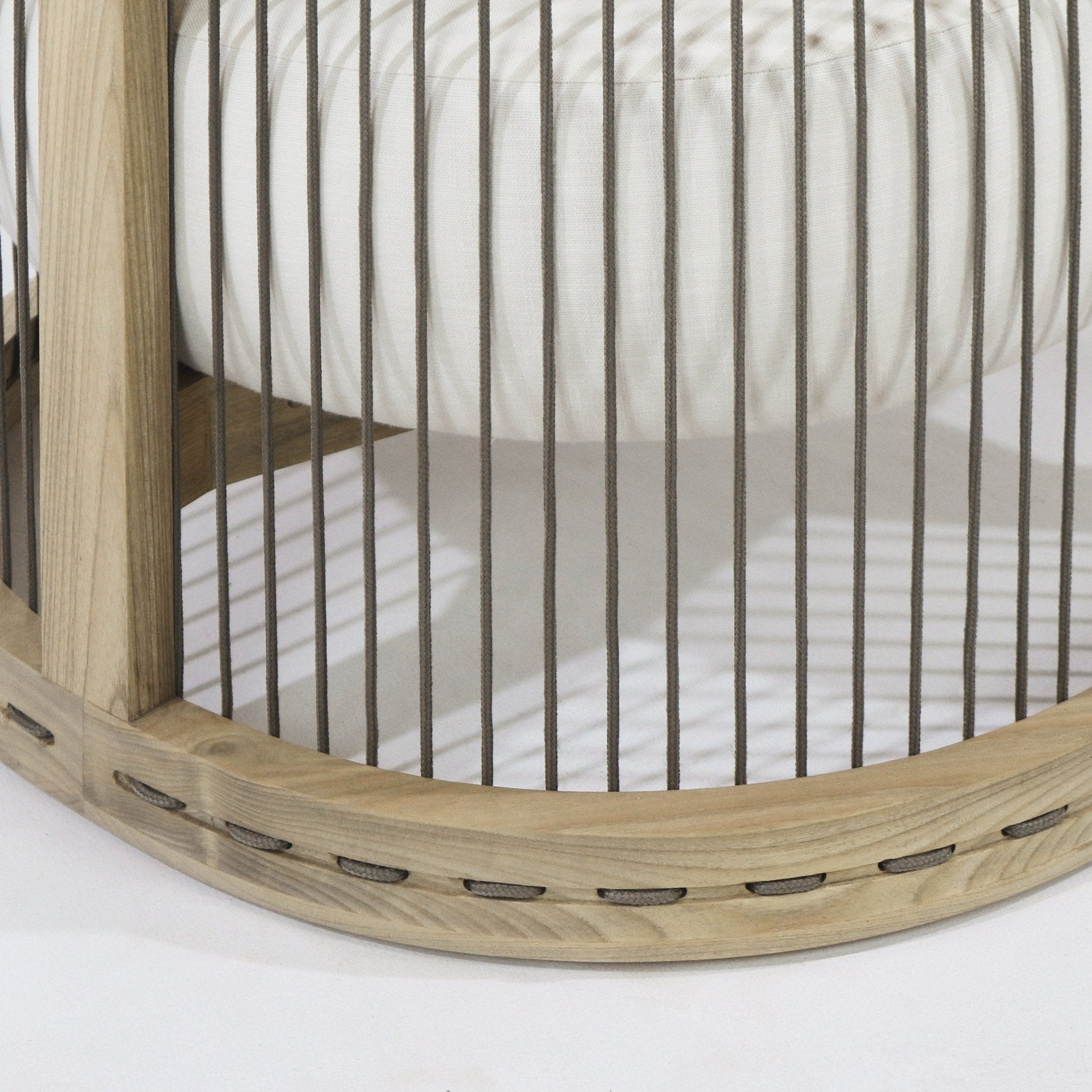 Close-up of a dining chair's light natural wood rounded base with vertical taupe rope back cords, showing the white fabric seat cushion above and woven rope threaded through the base.