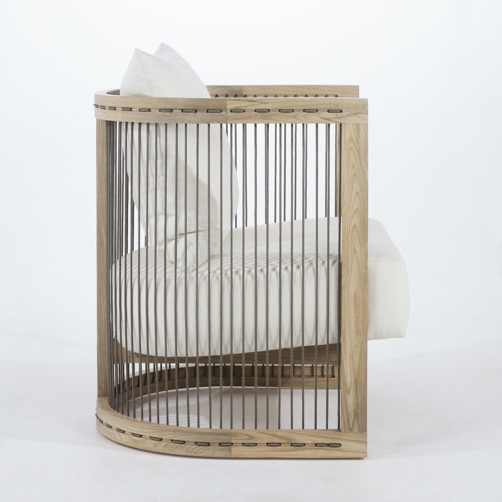 Side view of a modern dining armchair with a curved natural wood frame, vertical rope slats and a white fabric seat and back cushion.
