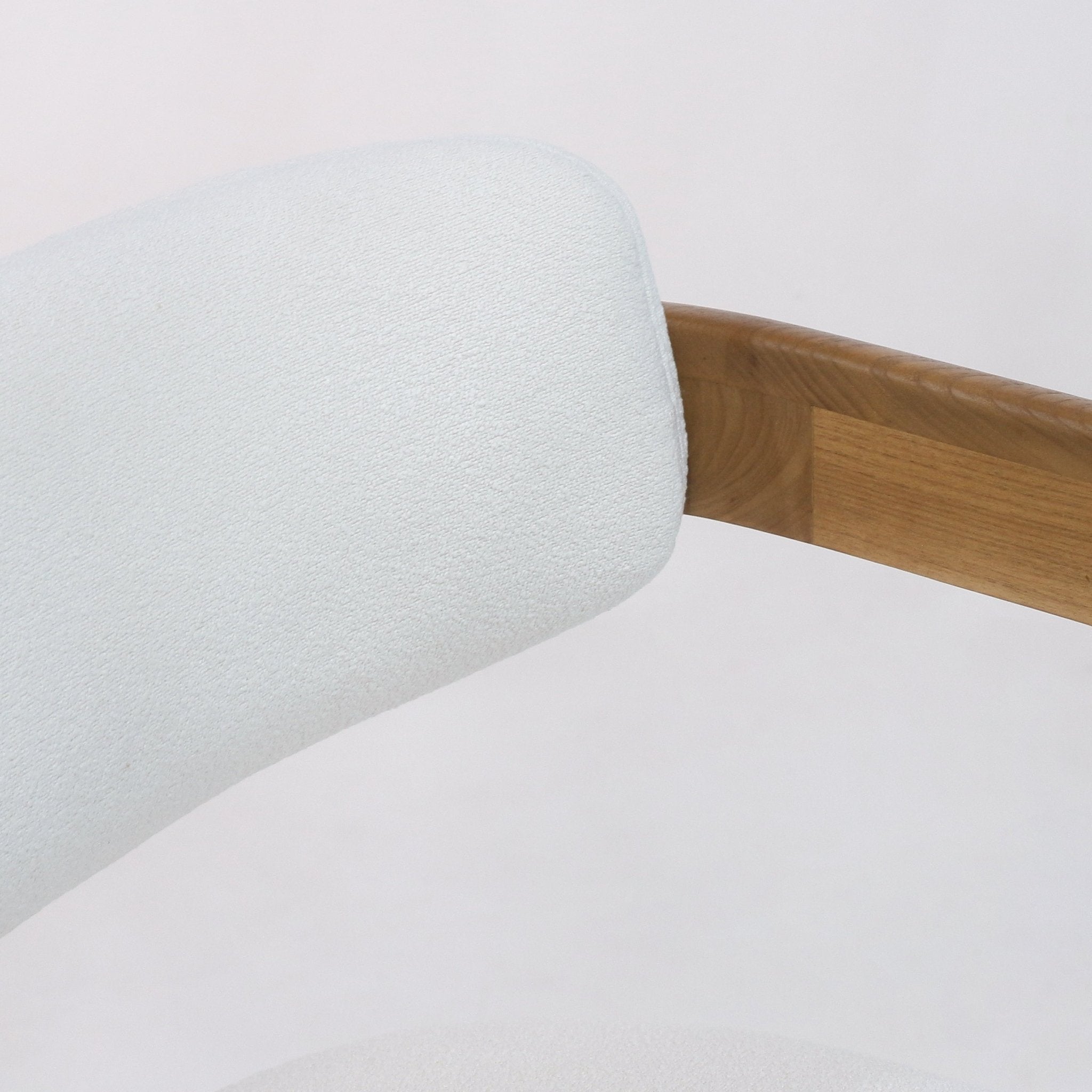 Close-up of a white boucle upholstered dining chair backrest joined to a curved teak wood arm rail, highlighting the soft boucle texture and warm natural wood grain.