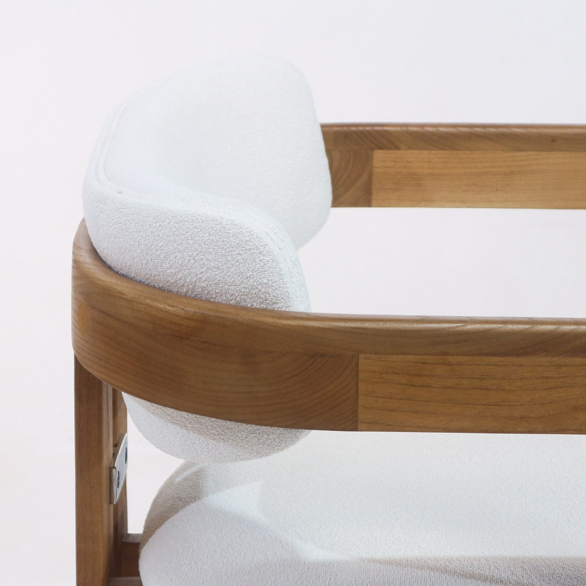Close-up of a mid-century modern teak-framed dining chair showing white boucle upholstery on the curved back and cushioned seat, highlighting natural wood grain and rounded arm detail.