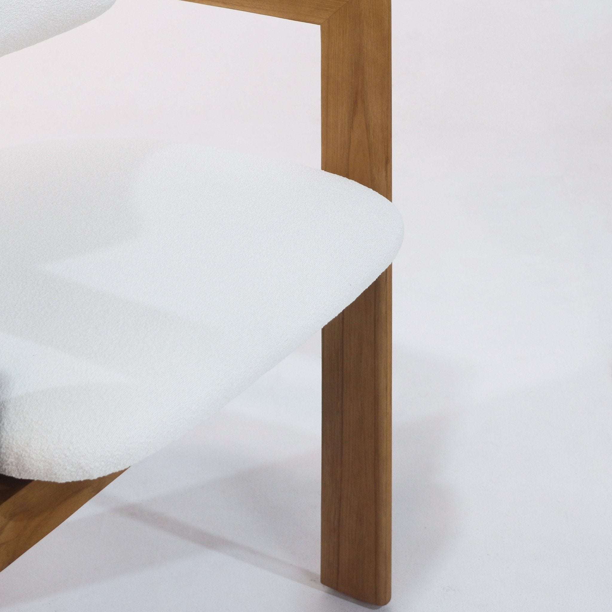 Close-up of a white boucle upholstered dining chair seat and teak wood leg, highlighting the rounded cushioned seat and mid-century modern teak frame.