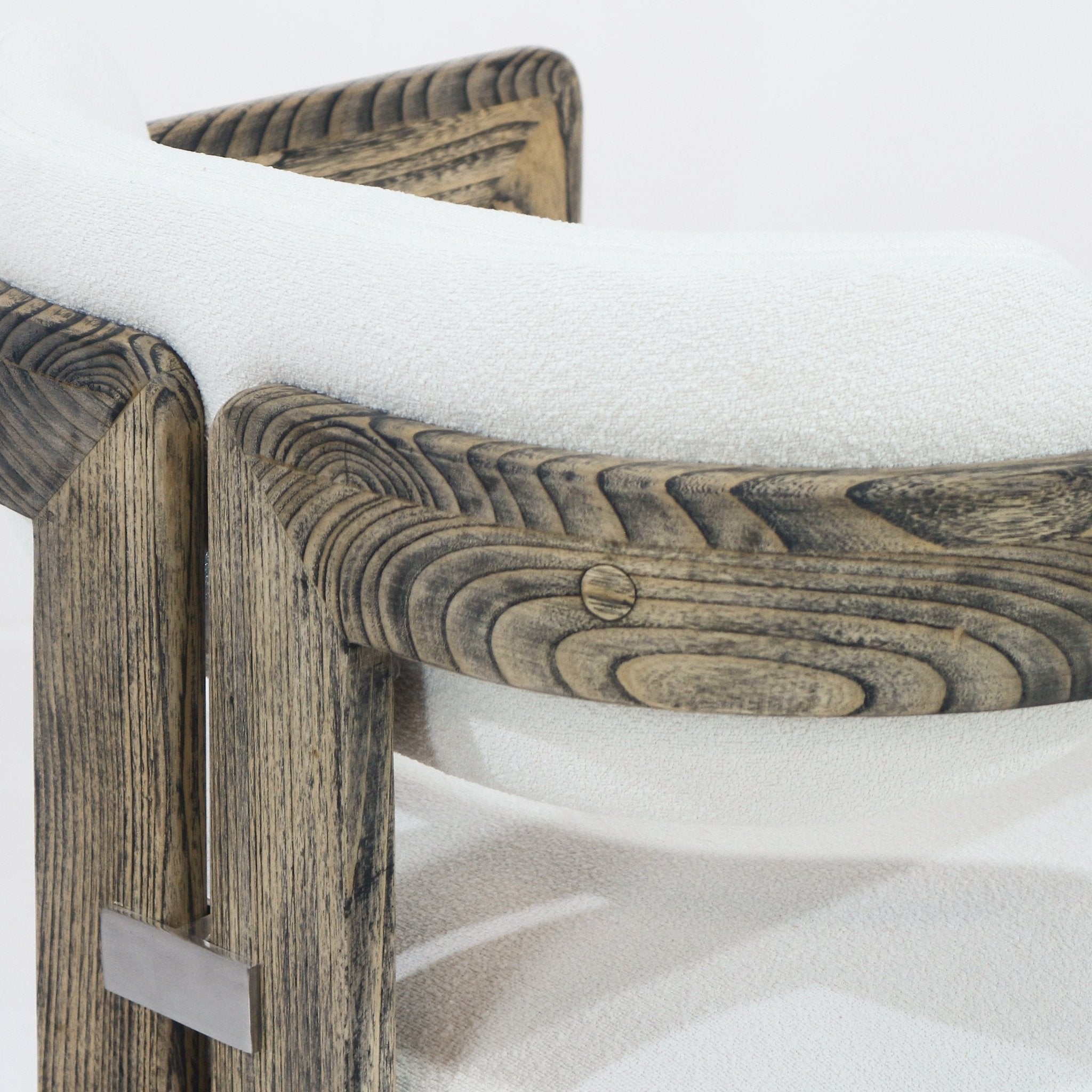 Close-up of a rustic natural wood chair arm and frame with pronounced brown grain, cream boucle upholstery on the seat and curved back, showing a round wooden peg and a rectangular metal accent plate.